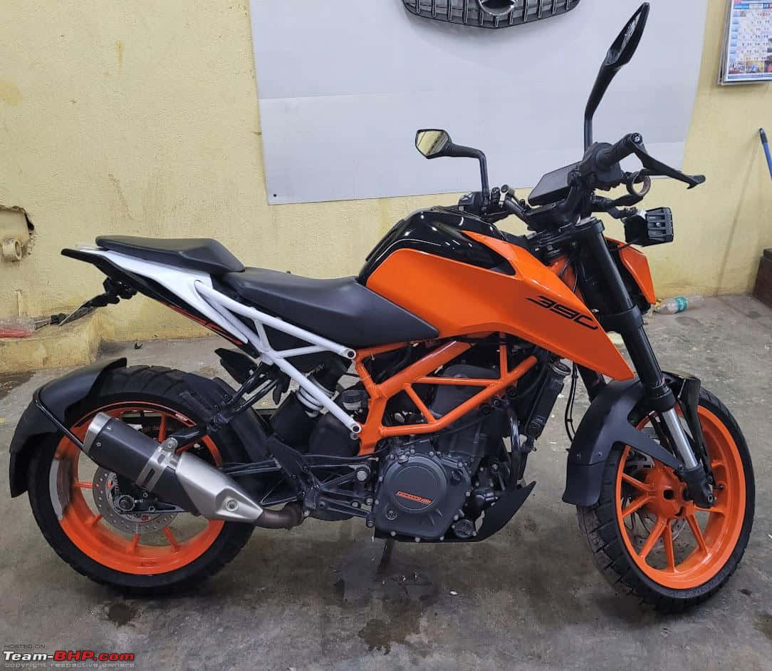 ktm bikes 桌布 壁紙 — 一輛鮮豔的橙色和黑色KTM 390摩托車停放在室內，靠著一面帶有白板的黃色牆壁。