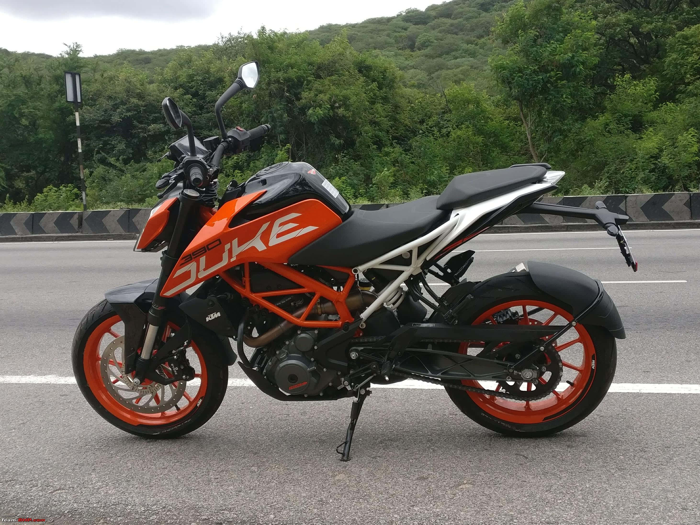 Road 桌布 壁紙 — 一輛鮮豔的橙色和黑色KTM Duke機車停在柏油路上，背景是翠綠的山丘。