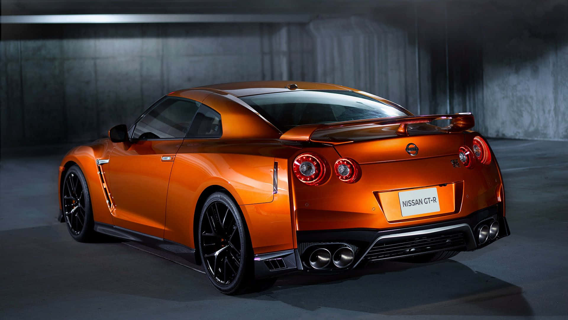 Gtr 桌布 壁紙 — 一輛鮮豔的橙色日產GT-R跑車在昏暗的混凝土車庫中以戲劇性的燈光從後方展示。