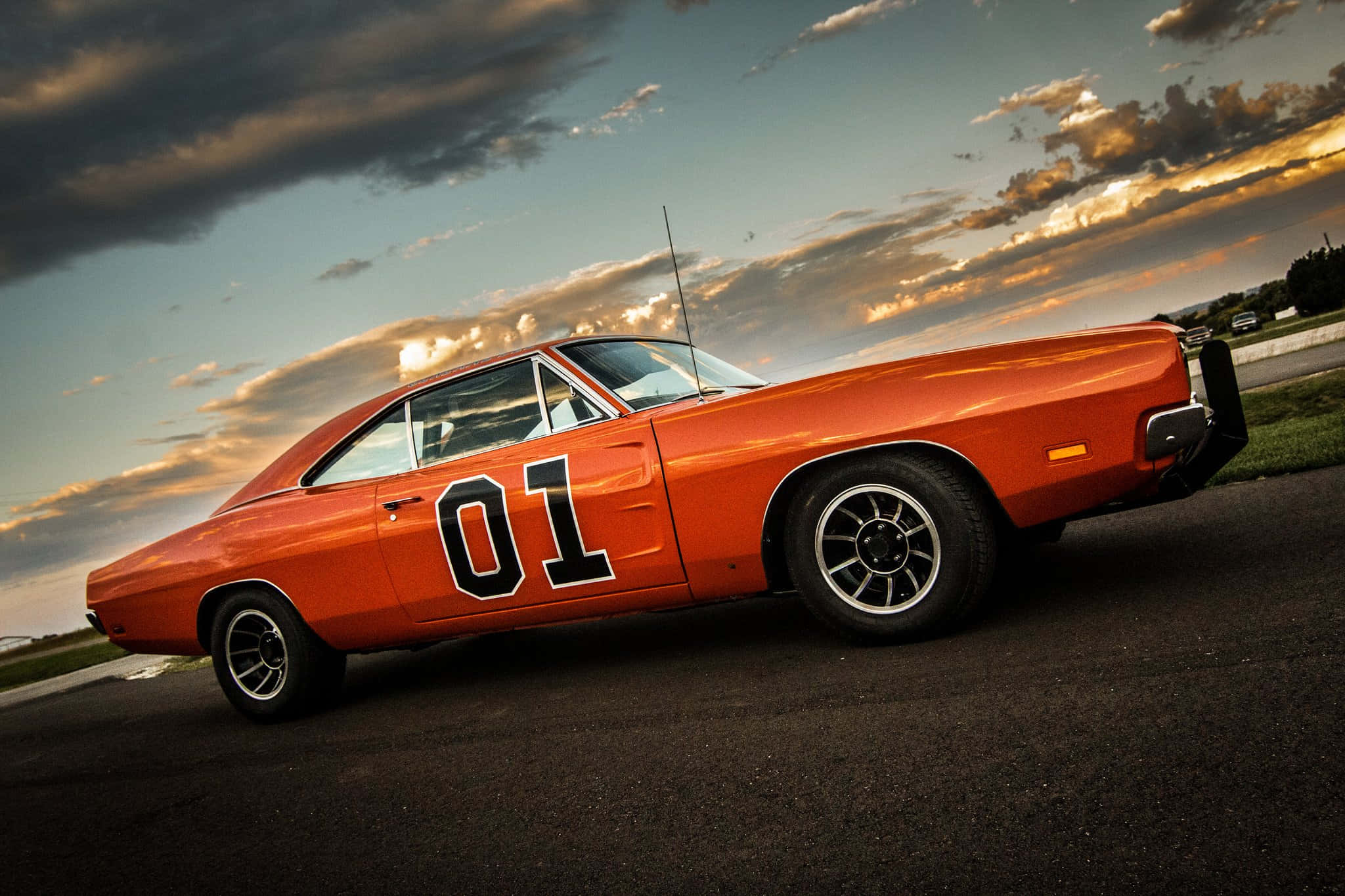 General Lee 車 桌布 壁紙 — 一輛鮮豔的橙色經典肌肉車，側面有「01」字樣，停在瀝青路上，背景是戲劇性的日落天空。