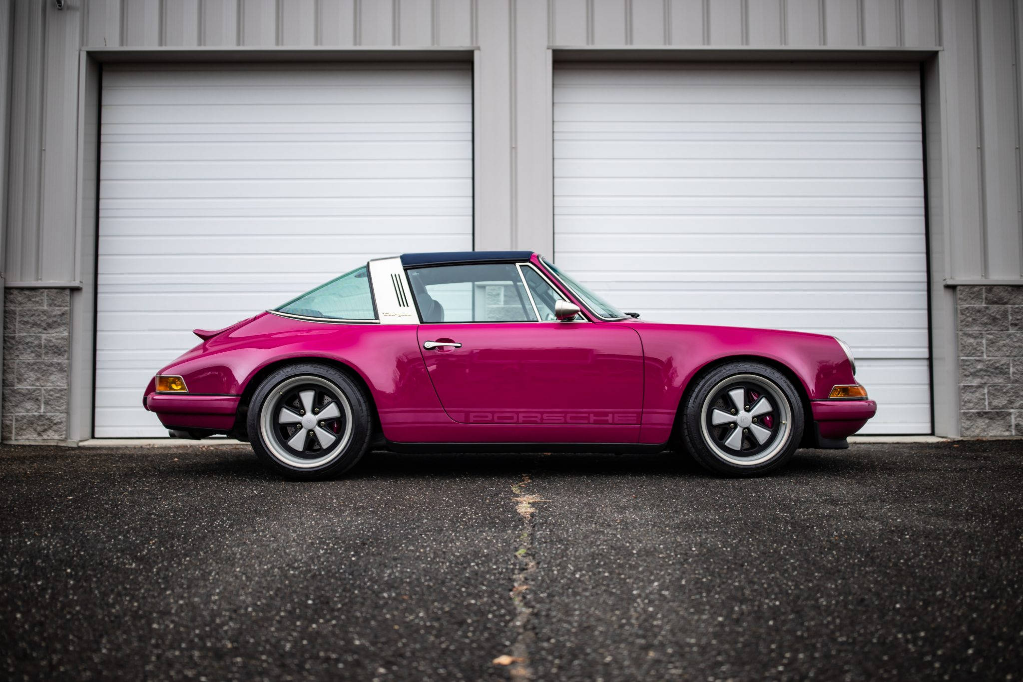 Singer 桌布 壁紙 — 一輛鮮豔的洋紅色保時捷911 Targa停放在灰色工業車庫門前的瀝青路面上。