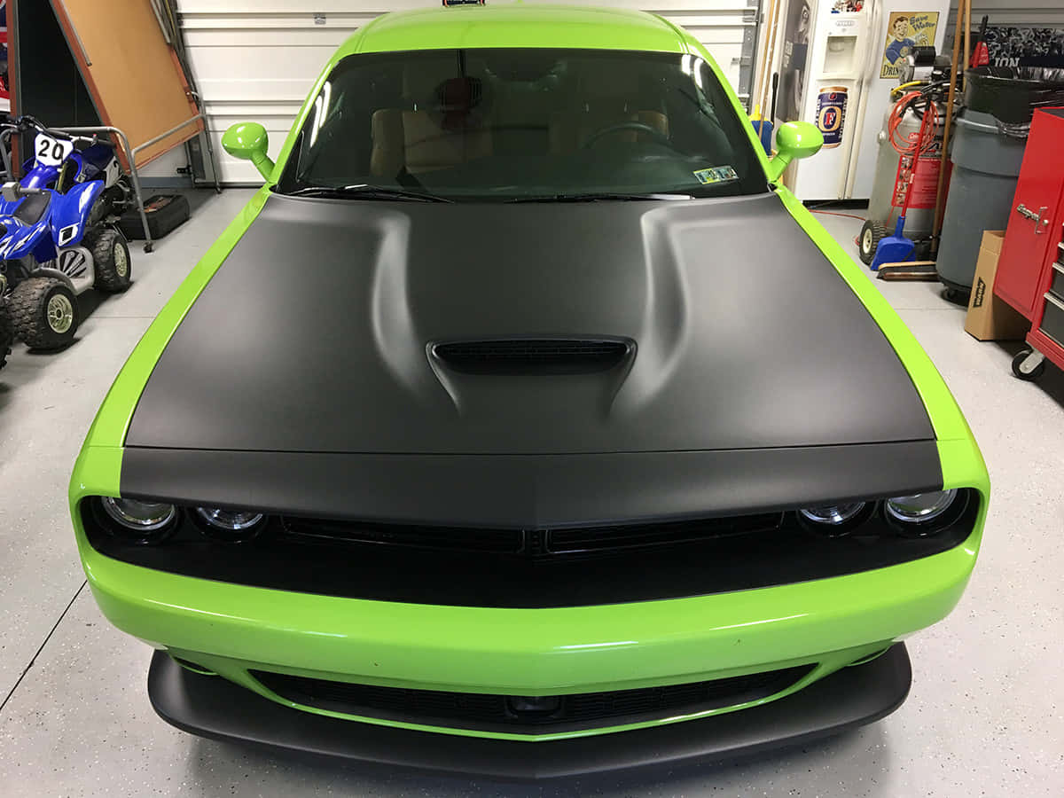 Car Hood 桌布 壁紙 — 一輛鮮豔的萊姆綠色 Dodge Challenger 配備消光黑色引擎蓋，醒目地停放在光線充足的車庫中，周圍有工具和一輛藍色 ATV。