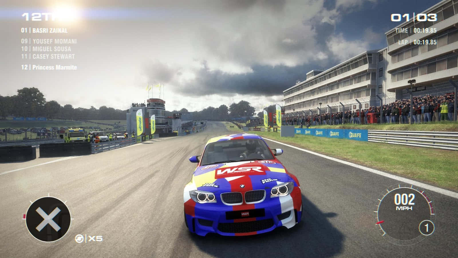 Grid 2 桌布 壁紙 — 一輛鮮豔的藍、紅、白色賽車在潮濕的賽道上奔馳，天空多雲，觀眾在看台上歡呼。