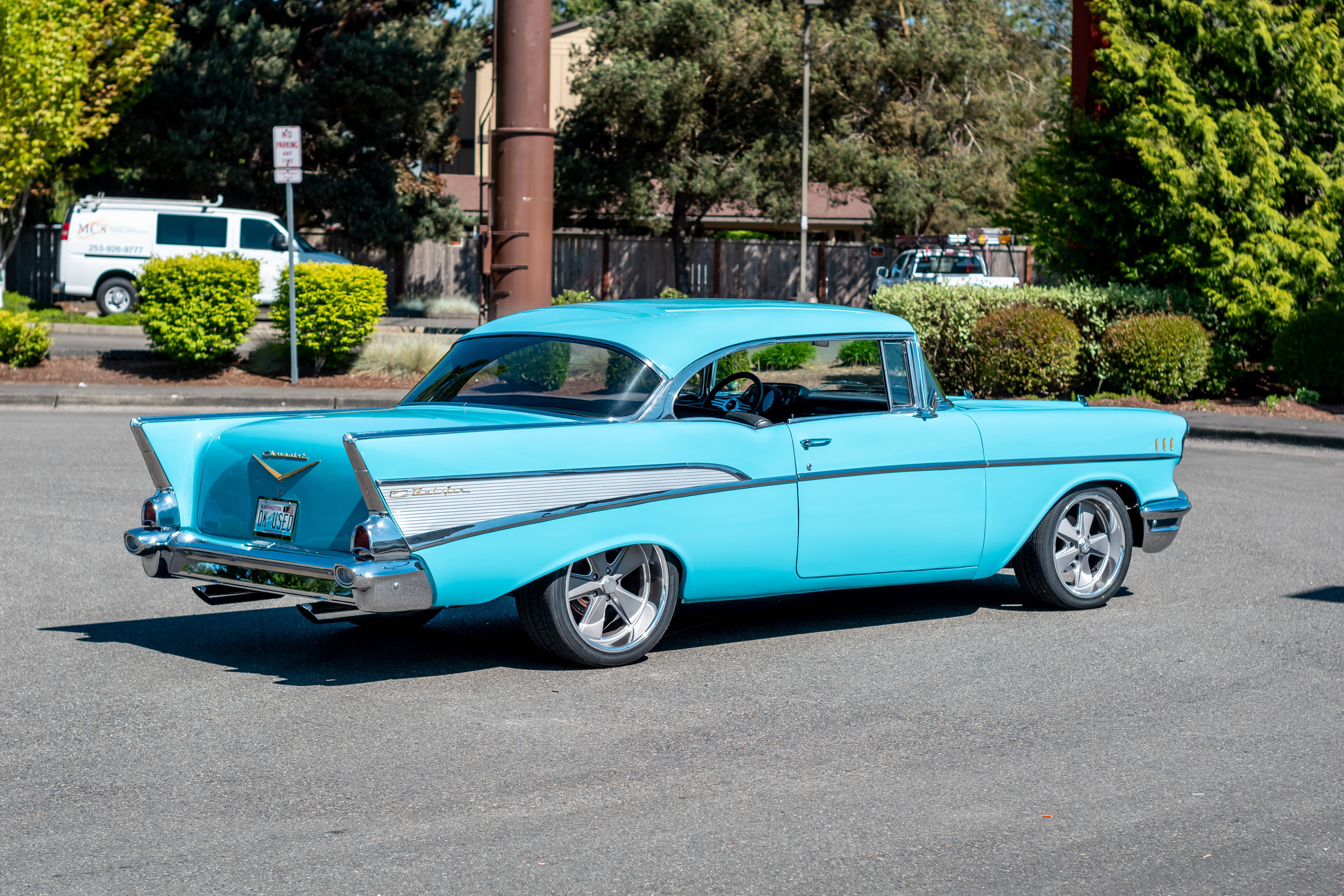 Chevrolet 桌布 壁紙 — 一輛鮮豔的藍綠色1957年雪佛蘭Bel Air在明亮的陽光下閃閃發光，停在一個被綠色樹木和灌木環繞的瀝青停車場上。