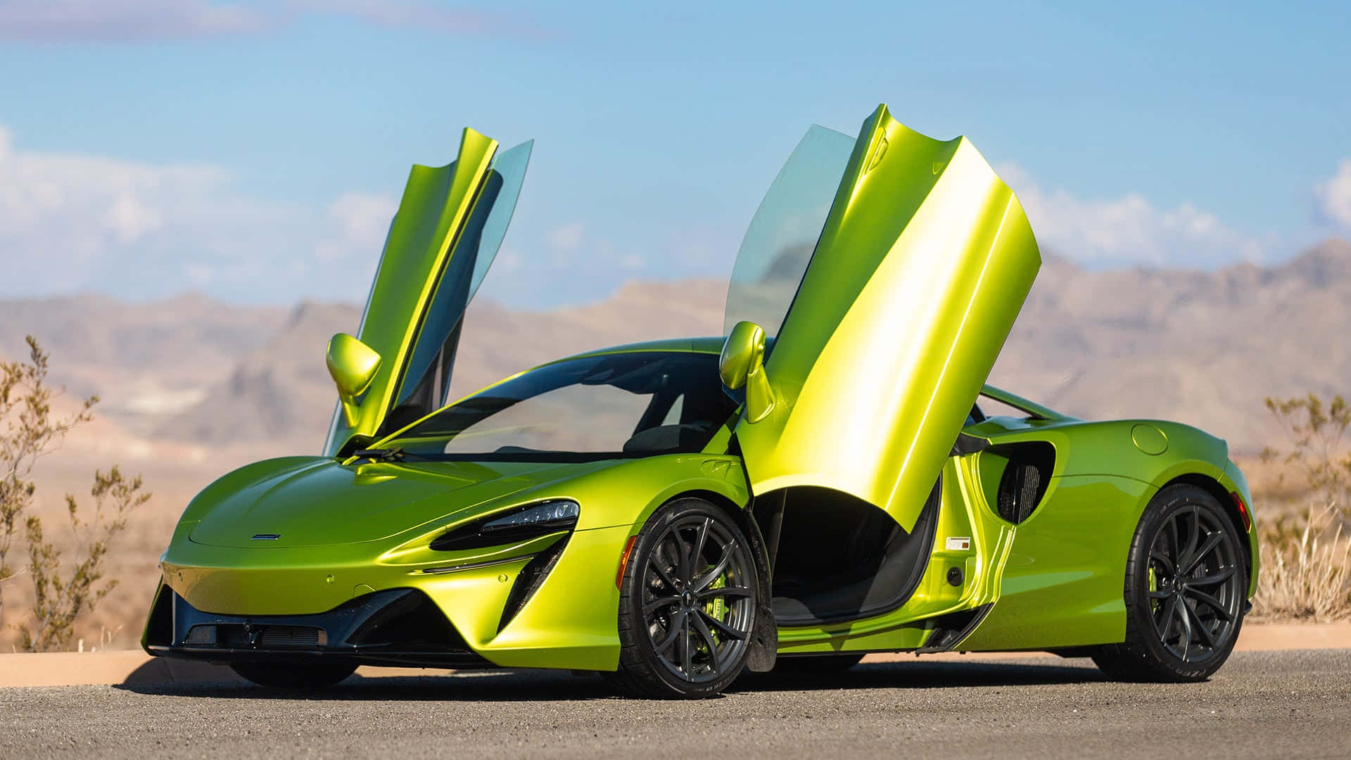 麥拉倫 桌布 壁紙 — 一輛鮮豔的青檸綠色McLaren跑車，鷗翼車門打開，停在沙漠公路上，背景是遠山和藍天。
