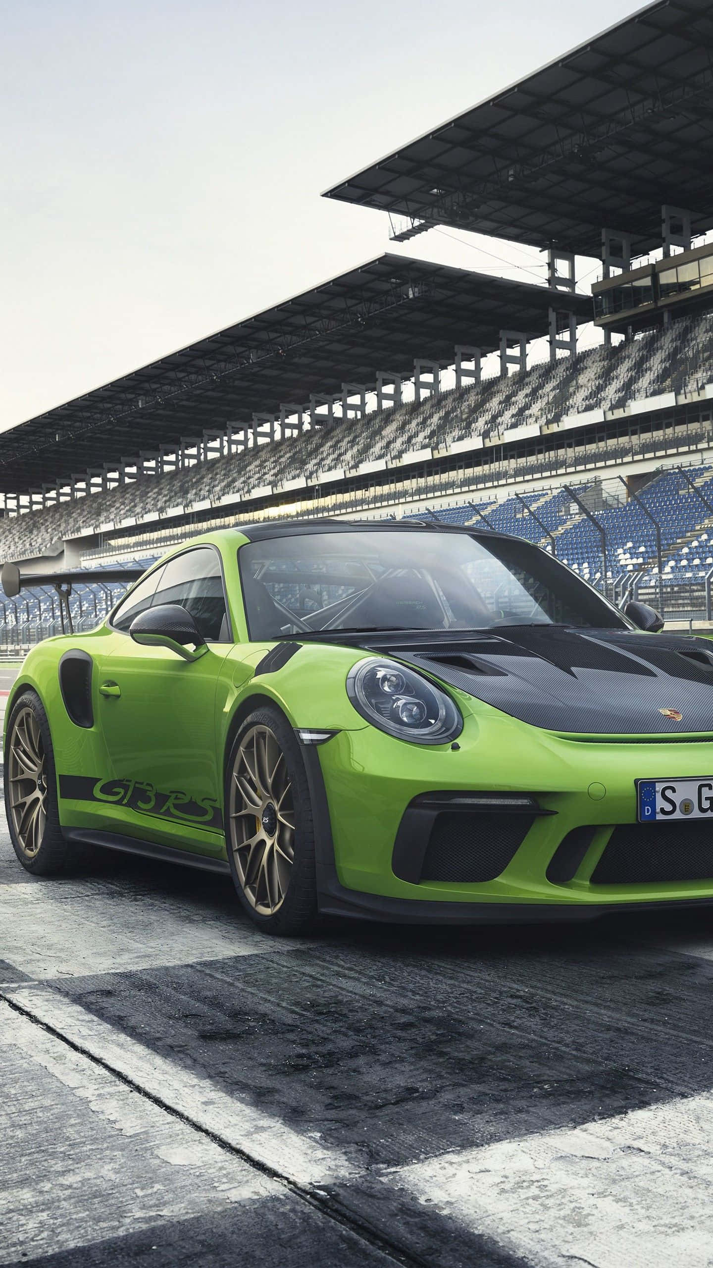 911 iPhone 桌布 壁紙 — 一輛鮮豔的青檸綠色保時捷911 GT3 RS在陰天之下停泊在濕滑的賽道上，背後是空無一人的看台。