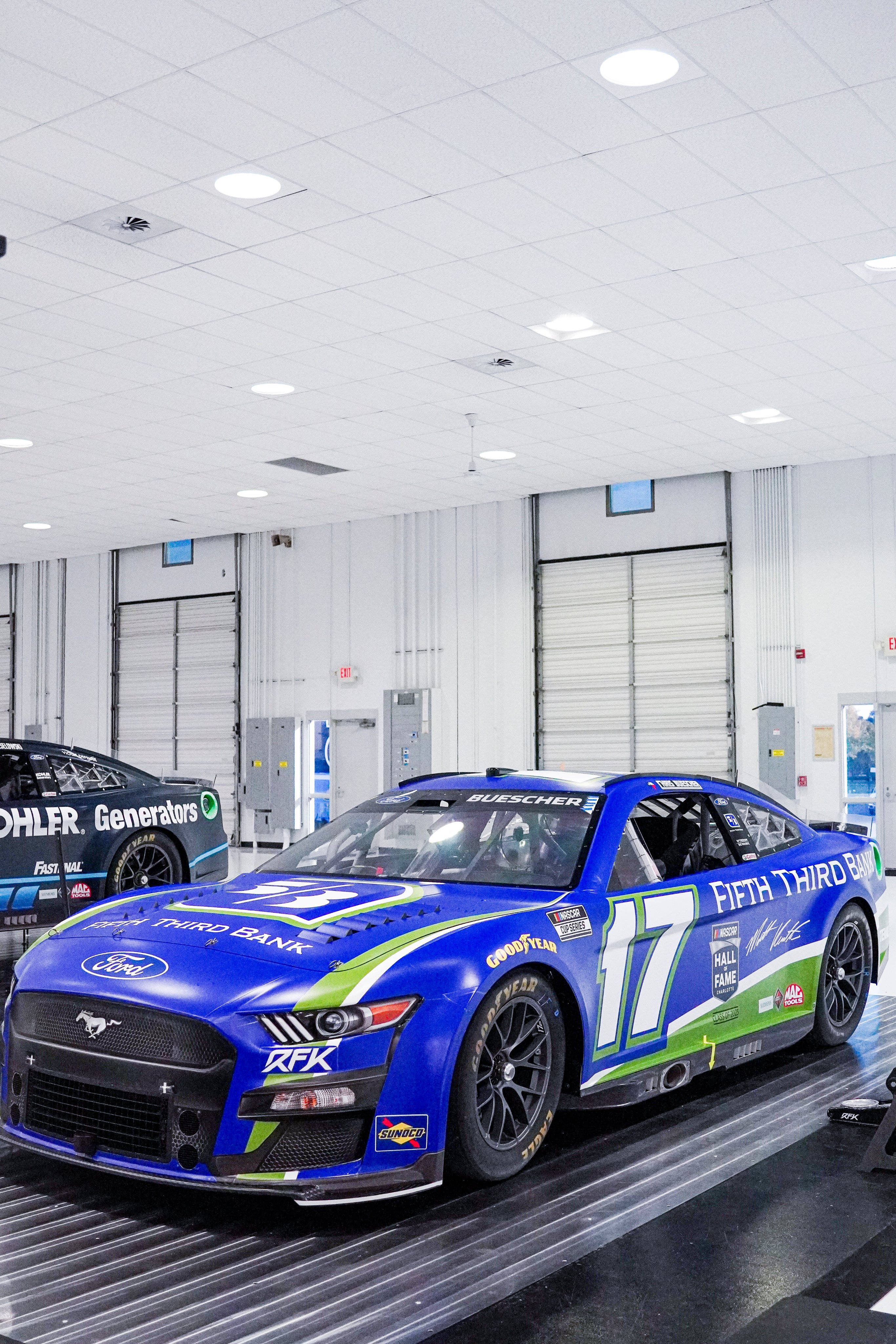 Ford Mustang 桌布 壁紙 — 一輛鮮豔藍綠色 #17 Ford Mustang 賽車帶有贊助商貼紙，停放在明亮潔淨車庫的升降台上。