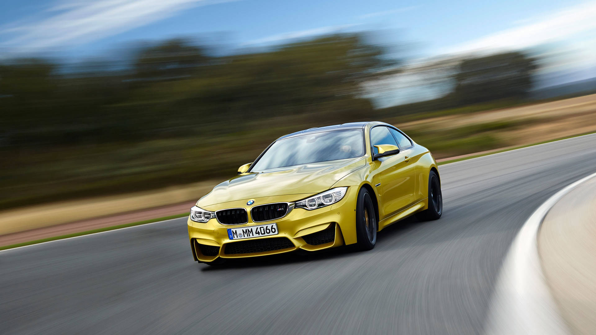 m 桌布 壁紙 — 一輛鮮黃色BMW M4 Coupe在彎曲的道路上疾馳，背景是模糊的綠樹和天空。
