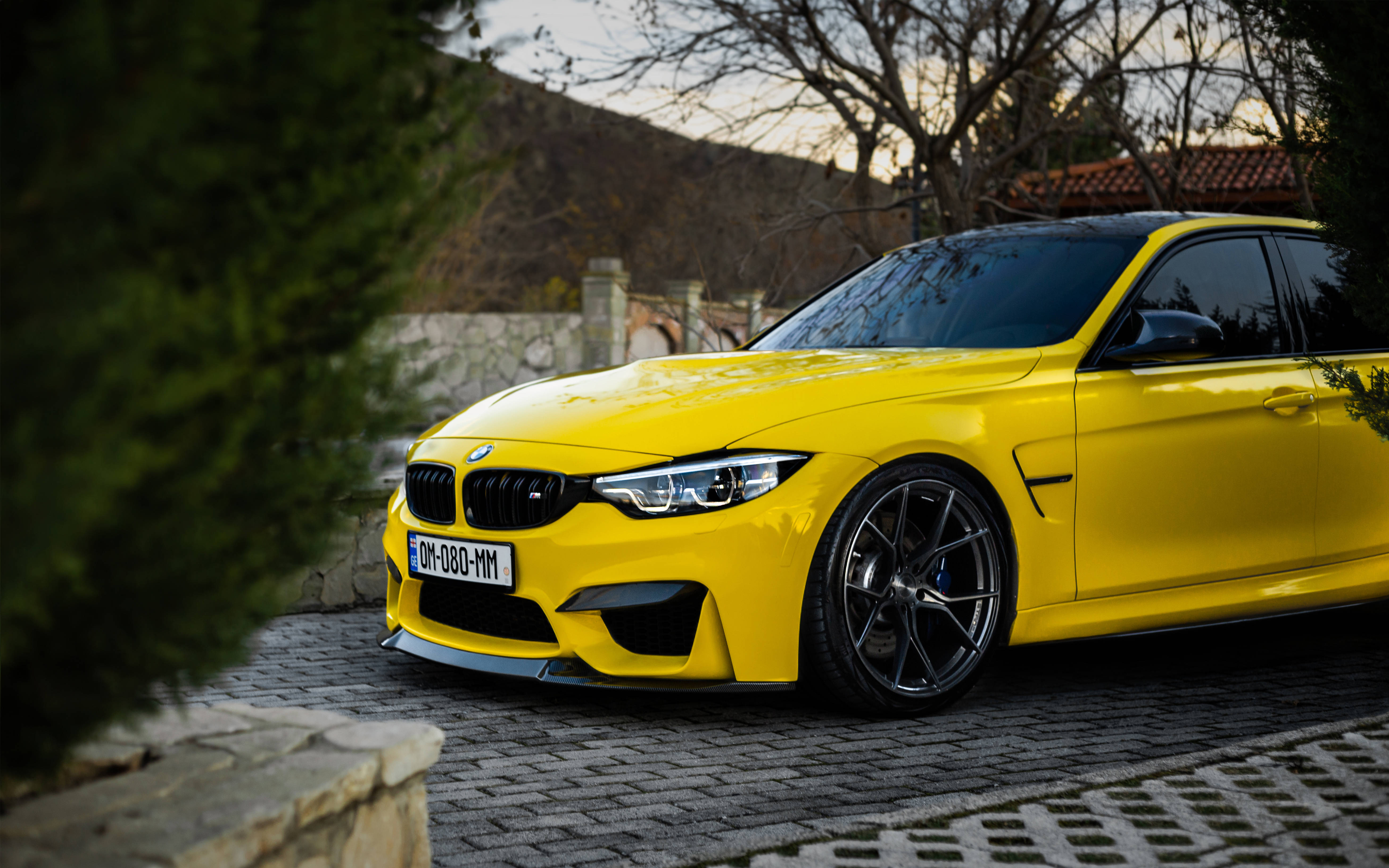 m 桌布 壁紙 — 一輛鮮黃色BMW M4跑車停泊在鵝卵石車道上，兩旁樹木環繞，正值黃金時刻。