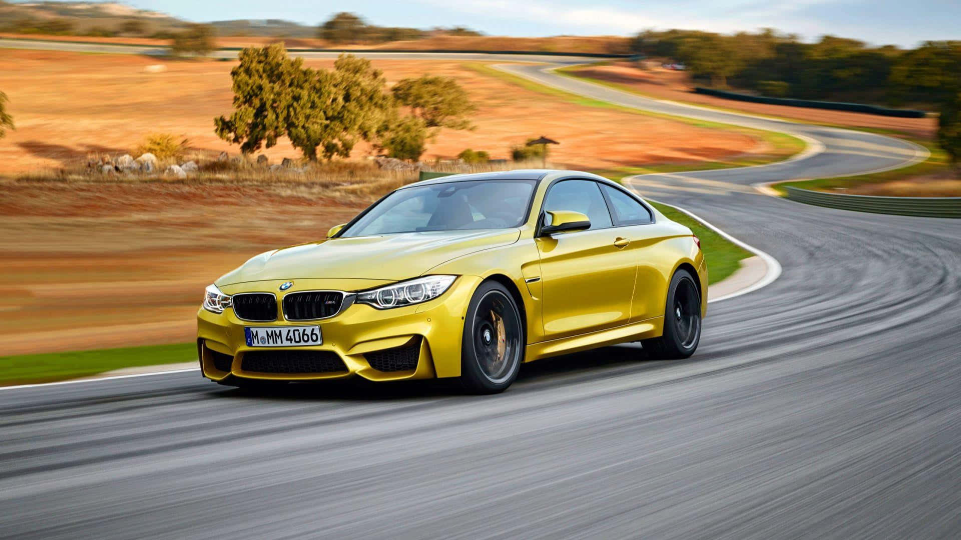 黃色BMW M4雙門跑車在彎曲道路上飛馳穿過乾燥鄉村。 — BMW 動圖 壁紙