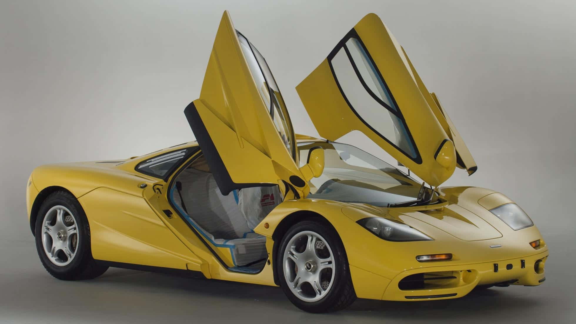 Mclaren F1 桌布 壁紙 — 一輛鮮黃色McLaren F1超級跑車，鷗翼車門打開，背景為中性攝影棚。