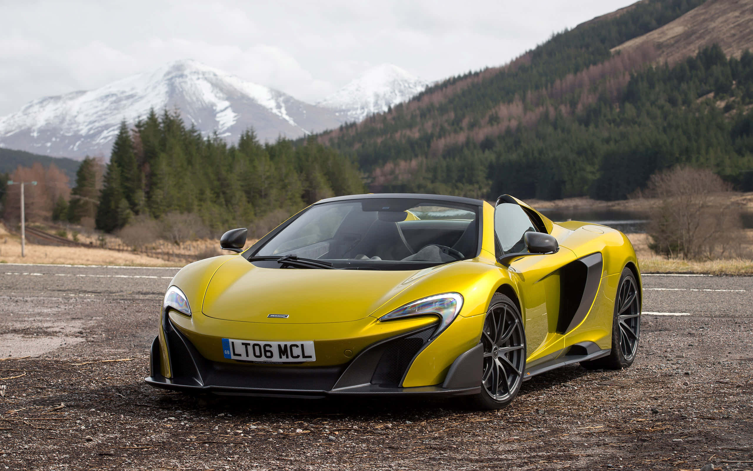Mclaren 675lt Spider 桌布 壁紙 — 一輛鮮黃色McLaren跑車停泊在碎石上，背景是白雪覆蓋的山脈和常綠森林。