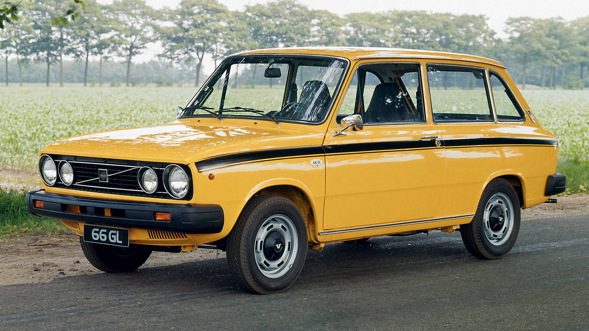 volvo iPhone 桌布 壁紙 — 一輛鮮黃色復古Fiat 126p旅行車停泊在鄉村道路上，旁邊是長滿高大綠色植物的田野。