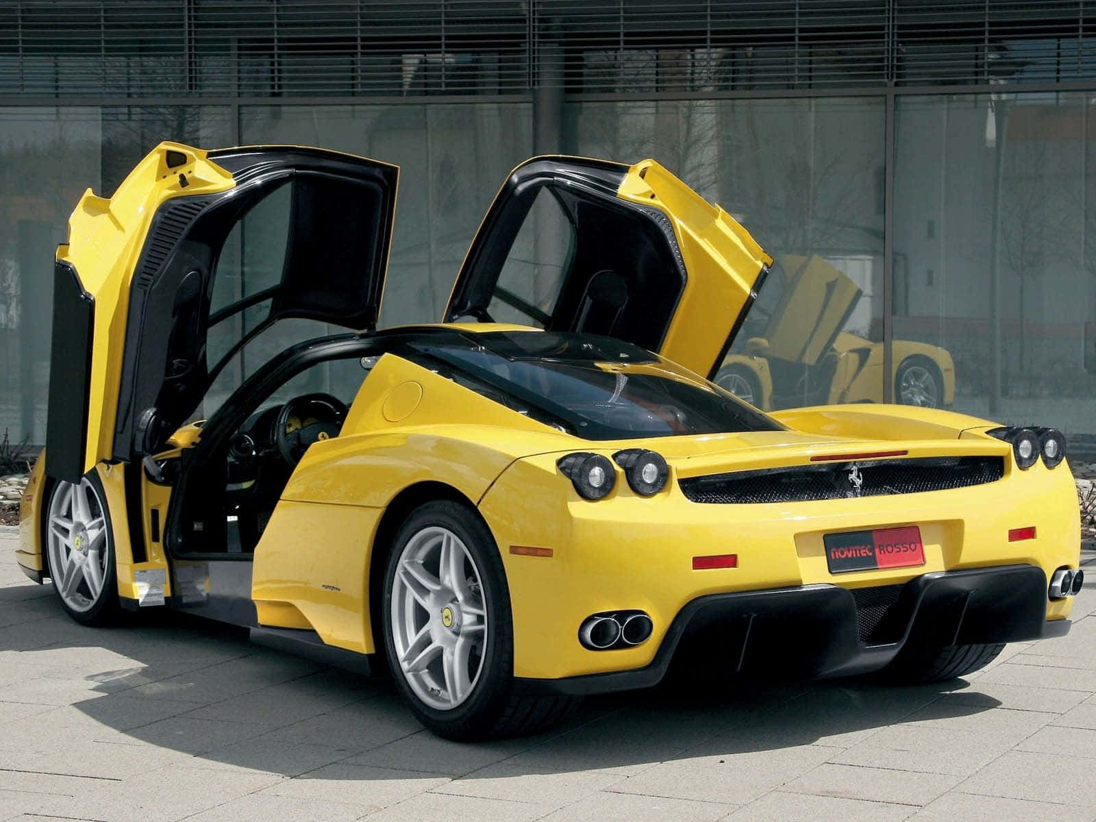 Yellow Car 桌布 壁紙 — 一輛鮮黃色法拉利Enzo，剪刀門打開，停放在現代玻璃建築前的鋪砌地面上。