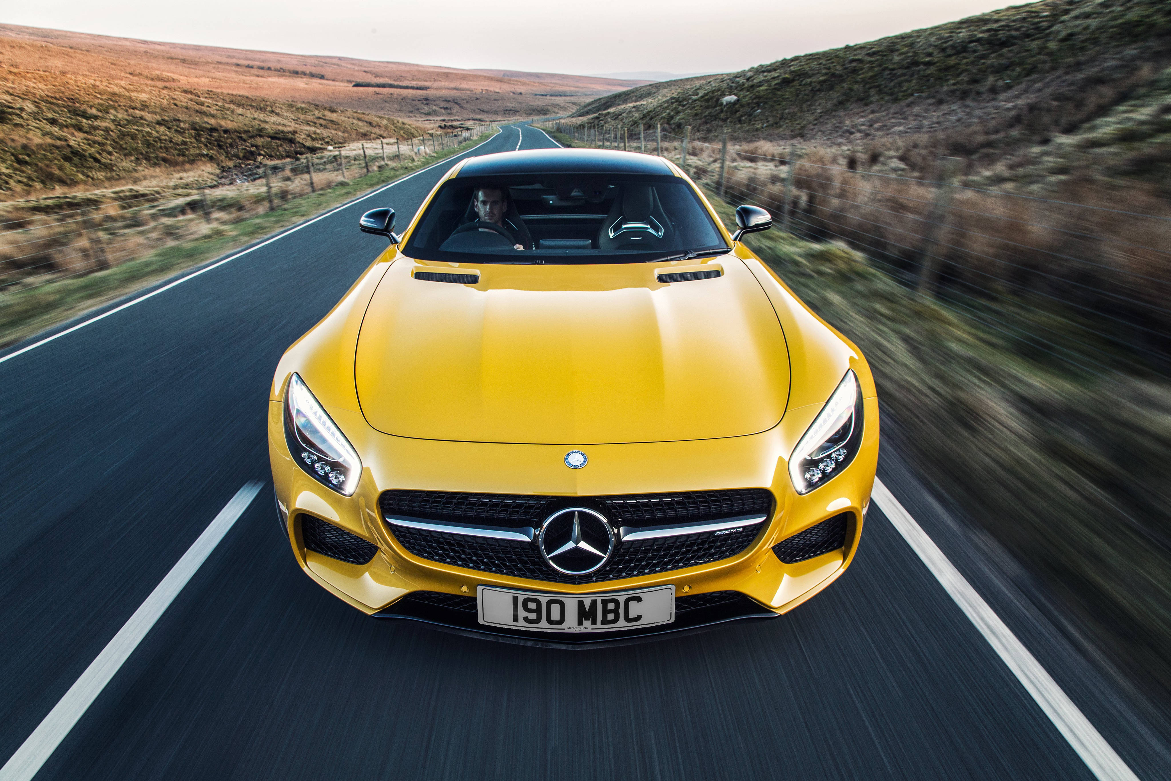 Mercedes 桌布 壁紙 — 一輛鮮黃色的 Mercedes-AMG GT 在蜿蜒的鄉村道路上疾馳，背景是模糊的動感和金色的山丘。