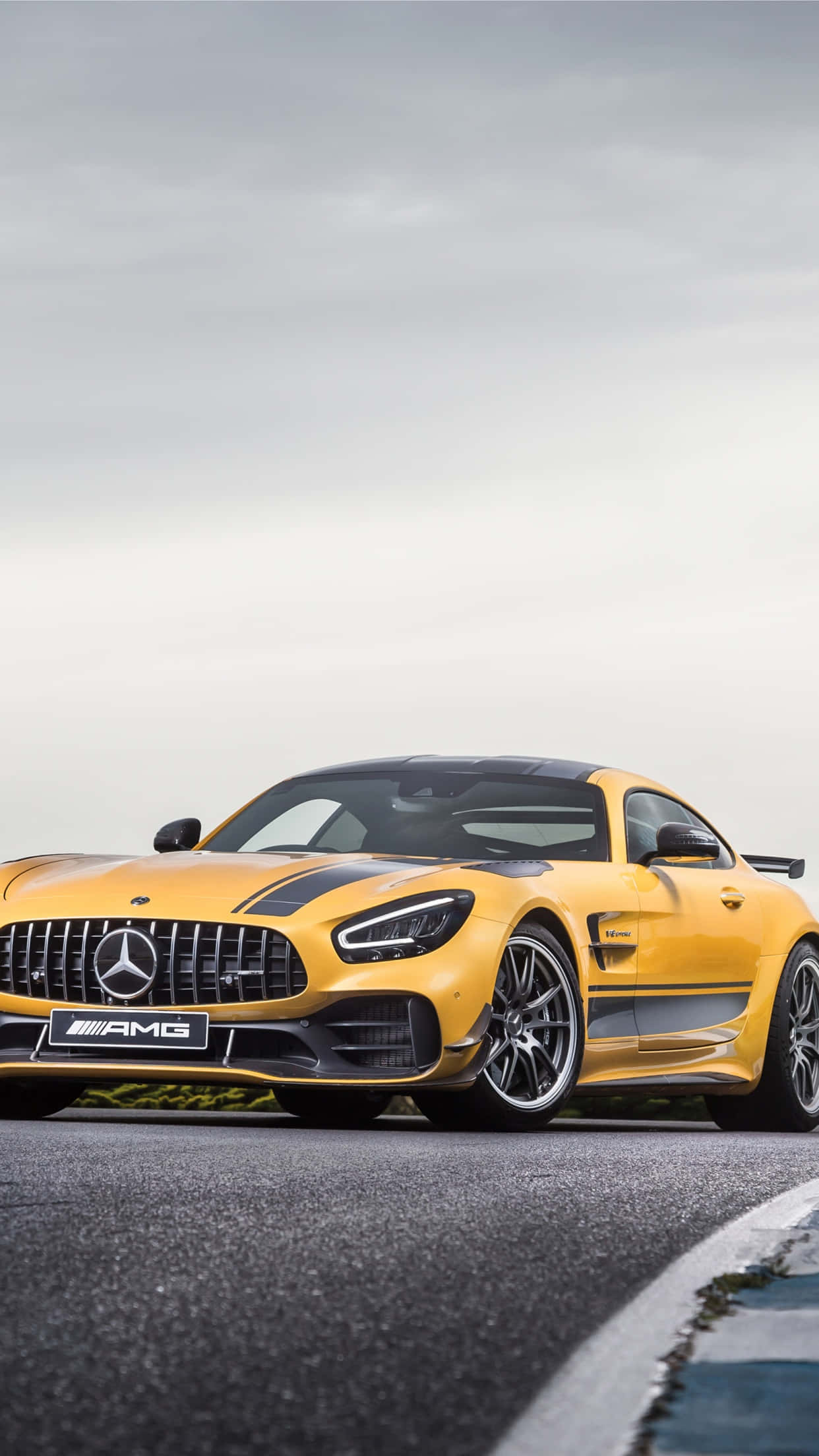 跑車 桌布 壁紙 — 一輛鮮黃色的 Mercedes-AMG GT R 跑車帶有黑色賽車條紋，停泊在陰天下的賽道上。