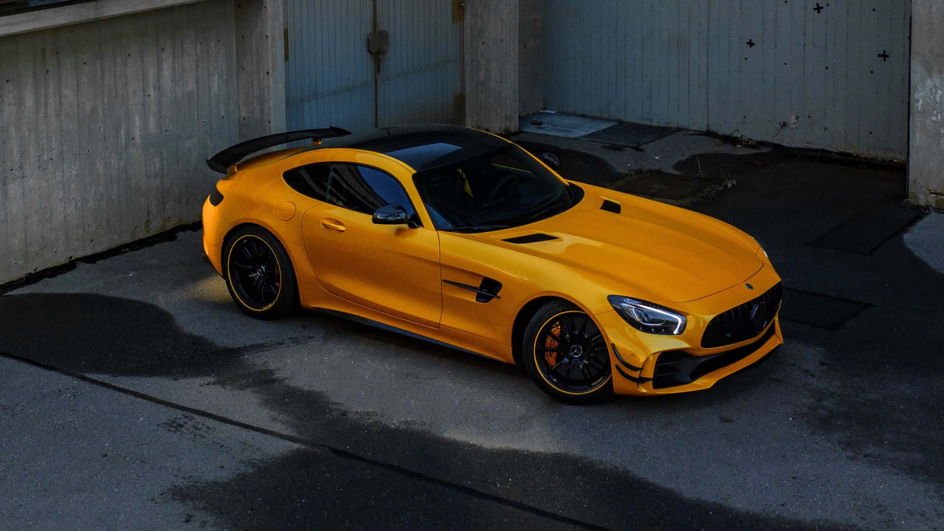 主題 桌布 壁紙 — 一輛鮮黃色的 Mercedes-AMG GT R 跑車停放在燈光昏暗的工業車庫中，車庫有混凝土牆壁和水窪。