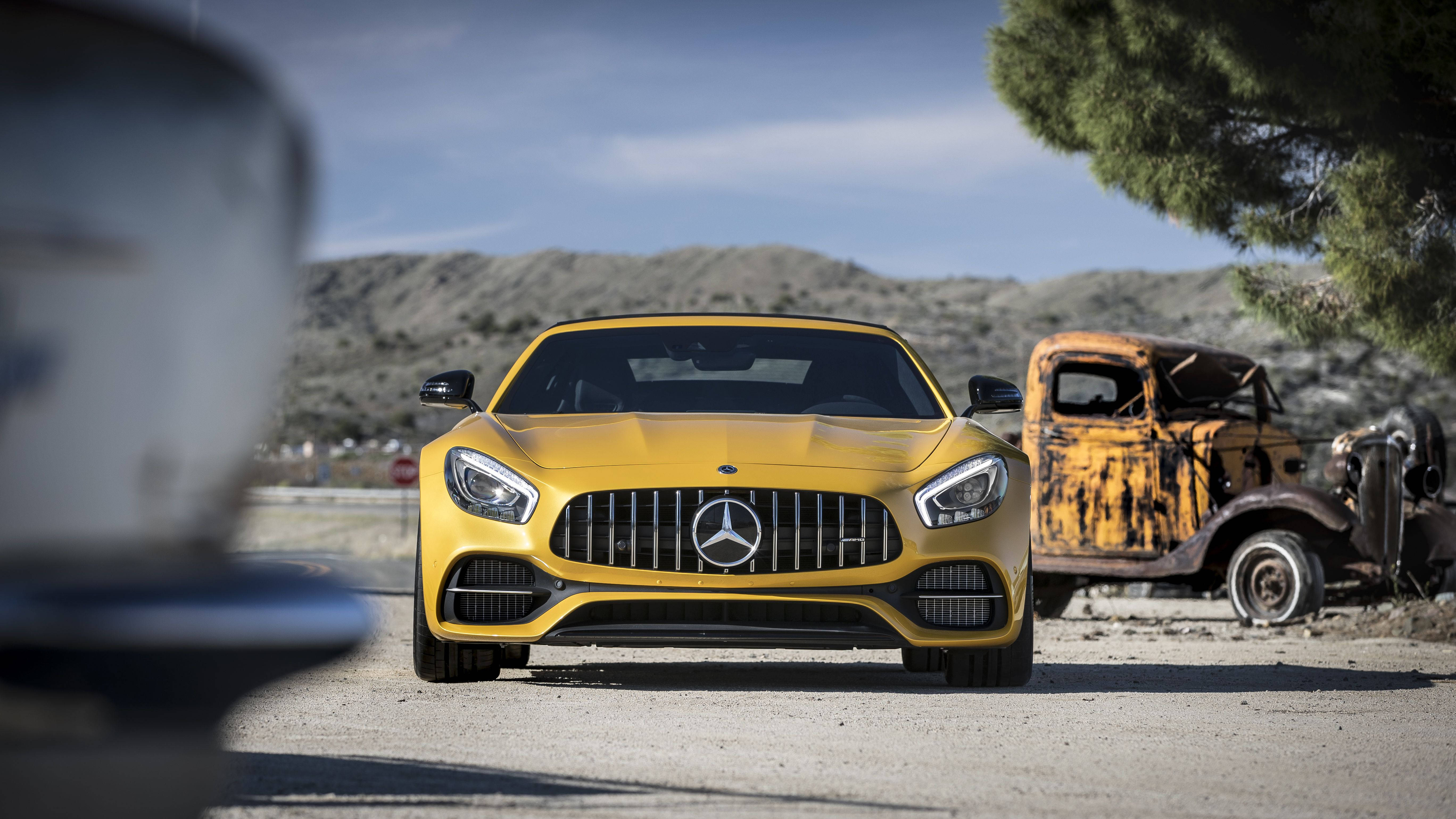 Gtr 桌布 壁紙 — 一輛鮮黃色的 Mercedes-AMG GT 跑車在塵土飛揚的道路上向前行駛，旁邊是一輛生鏽的復古卡車，背景是清澈的藍天。