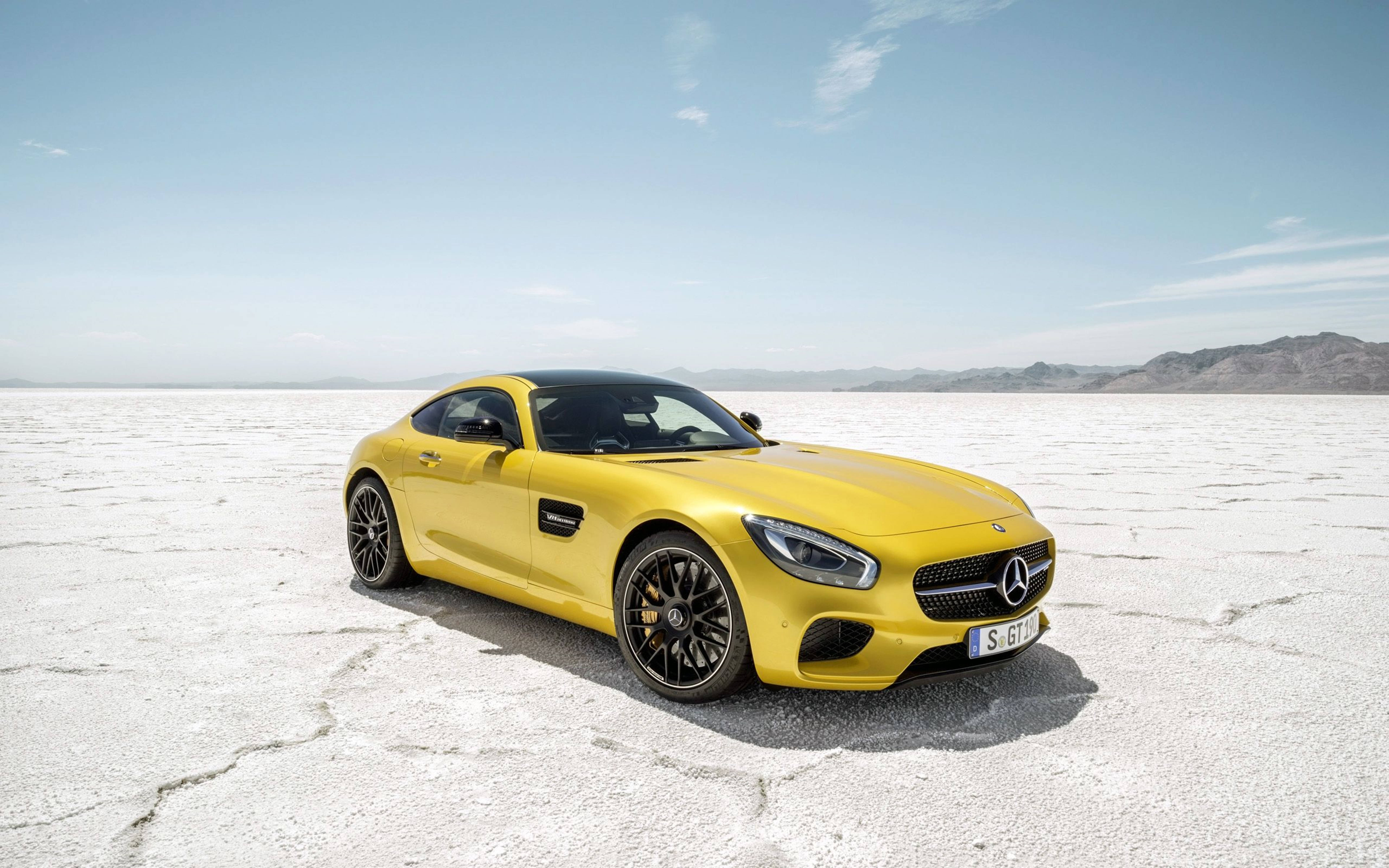 黃色 Mercedes-AMG GT S 在廣闊的鹽灘上，遠方有山巒。 — 4K 奔馳壁紙 壁紙