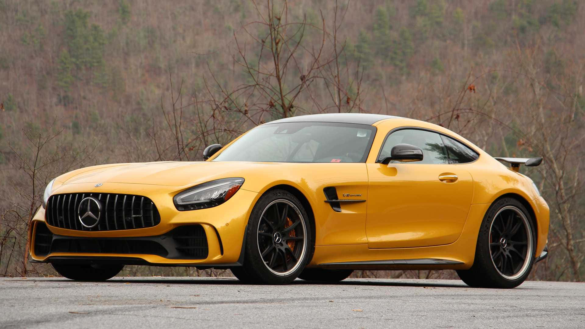 汽車 桌布 壁紙 — 一輛鮮黃色的 Mercedes-AMG GT R 跑車停在瀝青路上，背景是光禿禿的樹木和山丘。