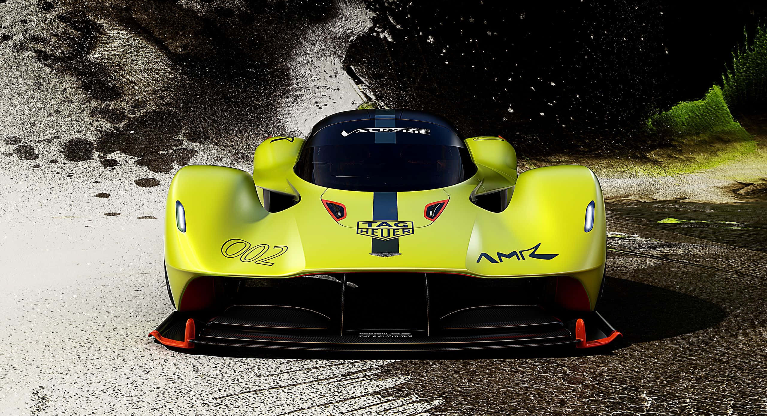 Aston Martin Valkyrie 桌布 壁紙 — 一輛鮮黃色的Aston Martin AMR1賽車在潮濕的賽道上疾馳，濺起戲劇性的水花，背景昏暗。