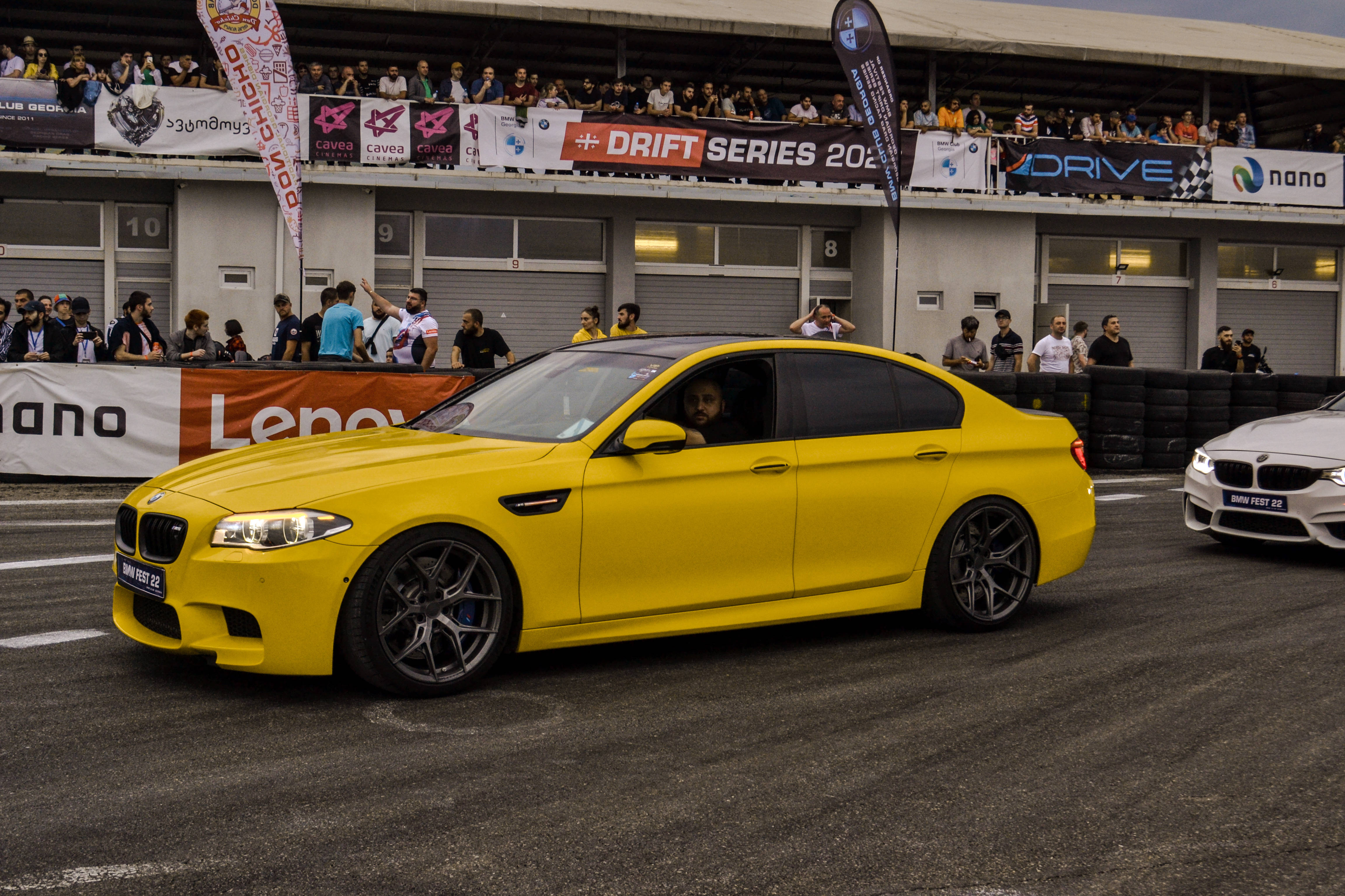 Racing 桌布 壁紙 — 一輛鮮黃色的BMW M5在賽車道上飄移，觀眾在陰天下的看台上觀看。