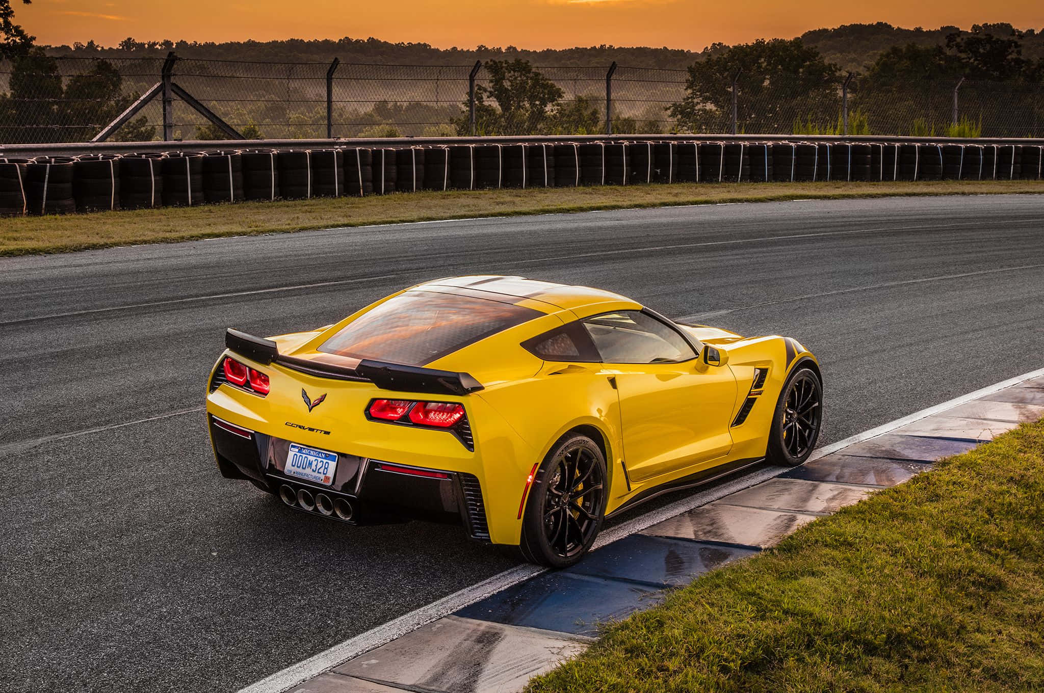 Chevrolet Corvette Grand Sport 桌布 壁紙 — 一輛鮮黃色的Corvette跑車停泊在賽車場上，背景是日落時分的橙色天空和輪胎護欄。