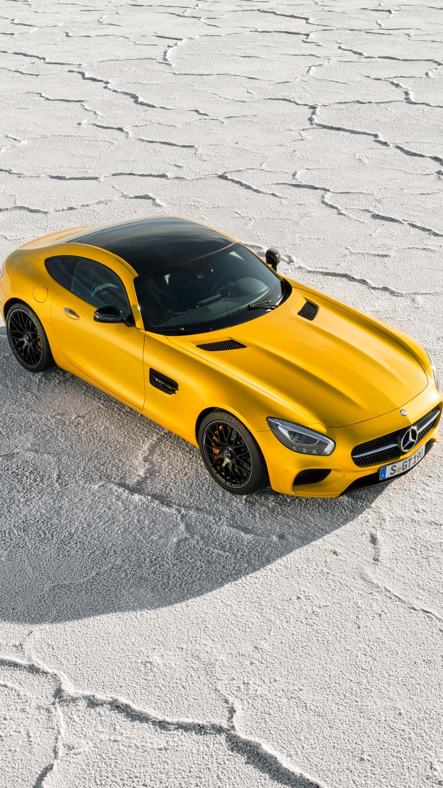 雪 桌布 壁紙 — 一輛鮮黃色的Mercedes-AMG GT跑車，配備黑色車頂和輪圈，停在龜裂的鹽灘上，在明亮的日光下。