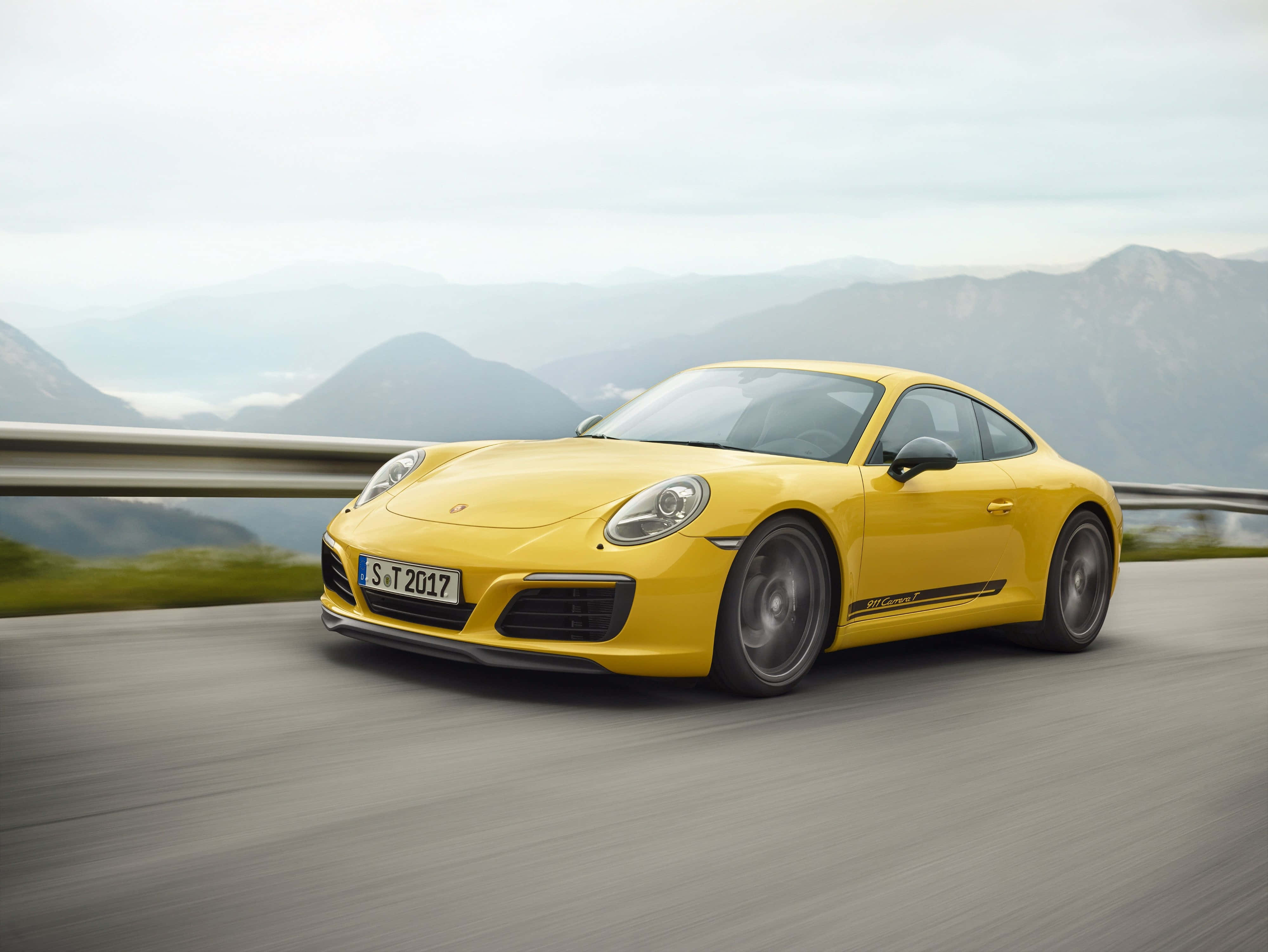 桌布 壁紙 — 一輛鮮黃色的保時捷911 Carrera T在霧氣繚繞的山峰背景下，沿著山路疾馳，呈現模糊動態。