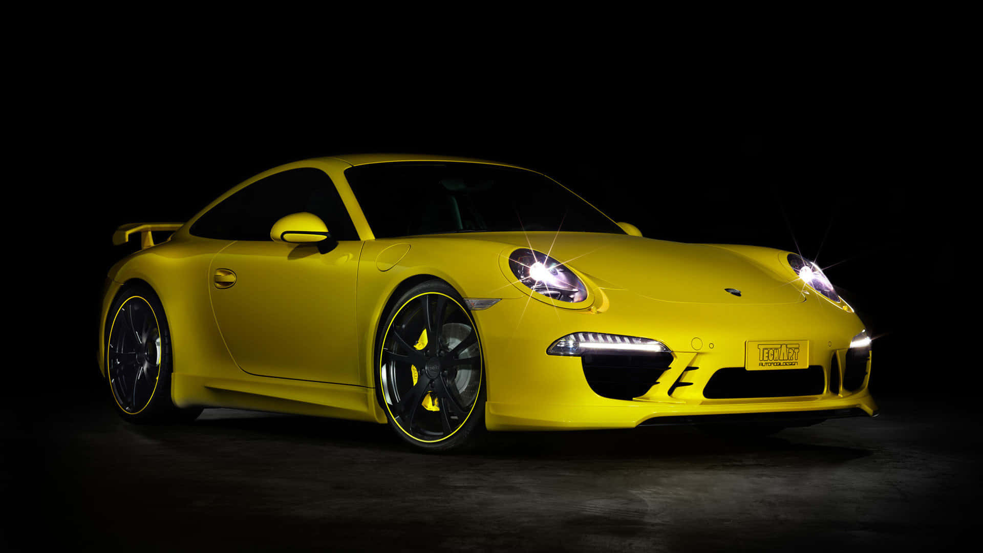 Yellow Car 桌布 壁紙 — 一輛鮮黃色的保時捷911 Turbo S在攝影棚燈光下閃閃發光，黑色背景襯托著發光的車頭燈。