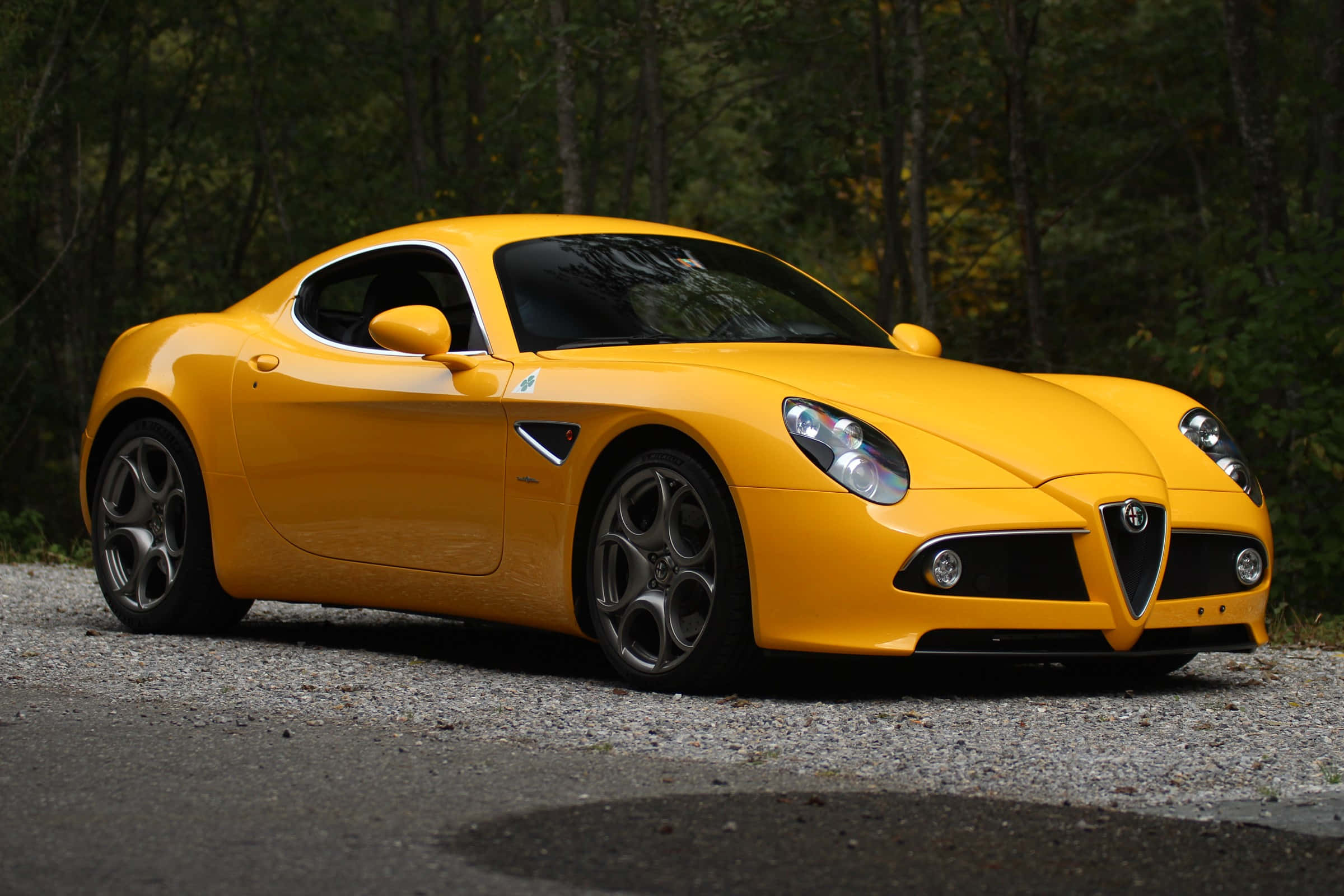 Alfa Romeo 8c Competizione 桌布 壁紙 — 一輛鮮黃色的愛快羅密歐跑車在碎石路上閃閃發光，周圍是茂密的秋日森林。