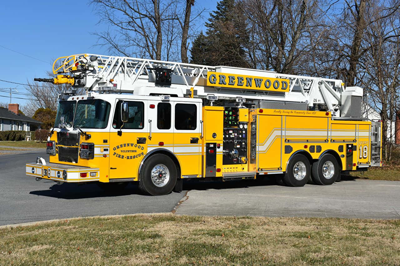 Fire Truck 桌布 壁紙 — 一輛鮮黃色的格林伍德志願消防救援雲梯車停泊在郊區街道上，天空湛藍清澈。