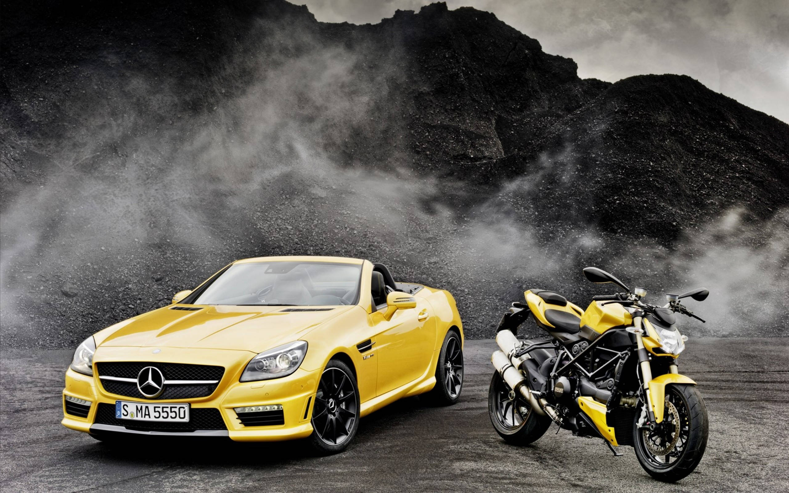 cars 桌布 壁紙 — 一輛鮮黃色的梅賽德斯 SLK 敞篷車和相配的杜卡迪摩托車並排站立在塵土飛揚的火山景觀中，天空風暴密佈。