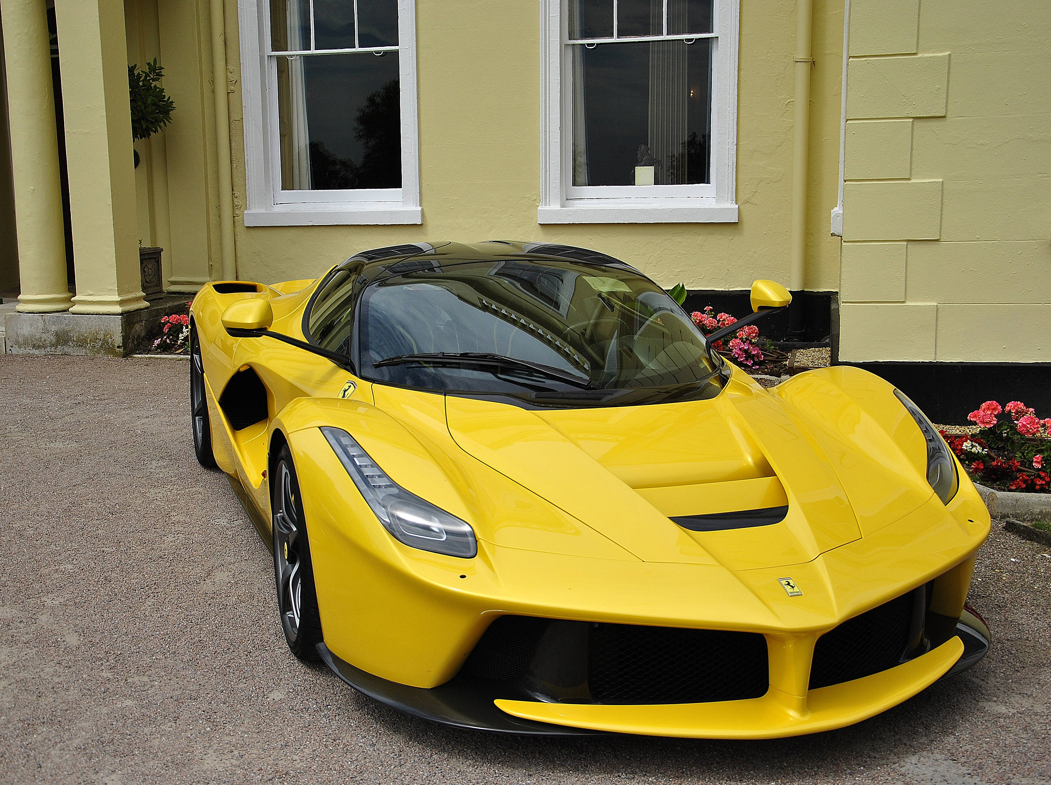 運動 桌布 壁紙 — 一輛鮮黃色的法拉利 LaFerrari 停放在碎石車道上，前方是一棟淺黃色房屋，帶有白色飾邊和花圃。