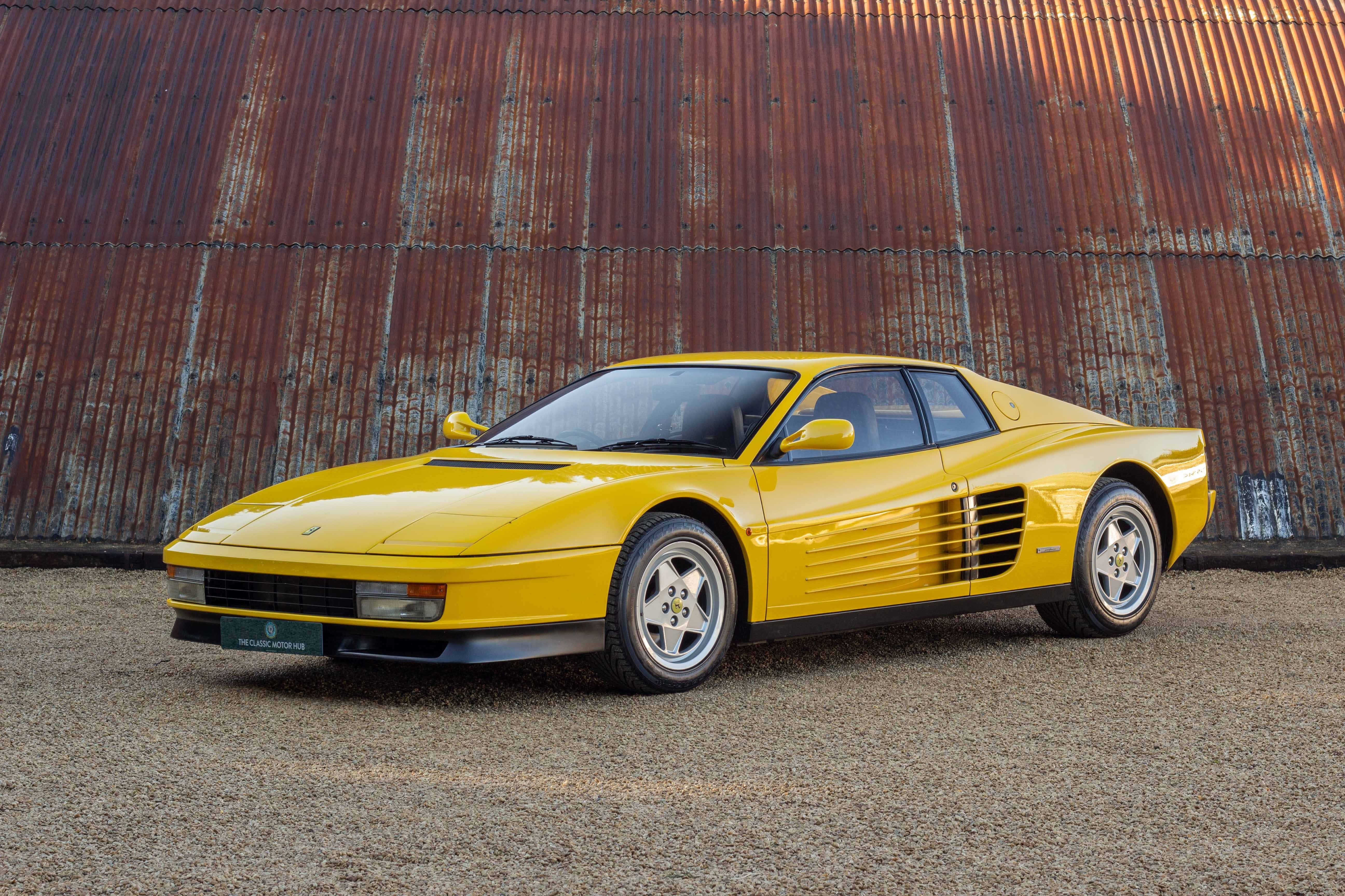 Ferrari Testarossa 桌布 壁紙 — 一輛鮮黃色的法拉利 Testarossa 在黃金時段的光線下，對著風化生鏽的金屬牆閃閃發光。