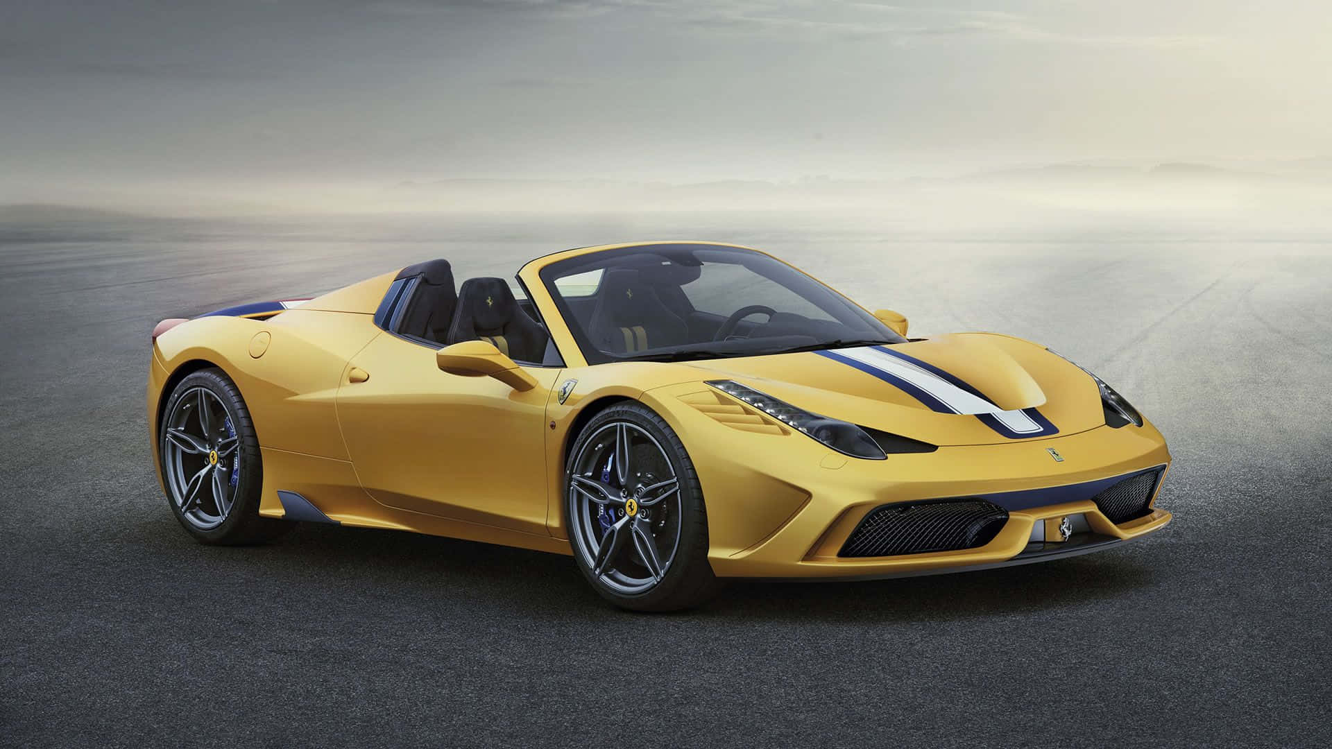 Ferrari 458 Speciale 桌布 壁紙 — 一輛鮮黃色的法拉利458 Spider，帶有黑色賽車條紋，在霧氣瀰漫的瀝青賽道上，於柔和日光下閃閃發光。