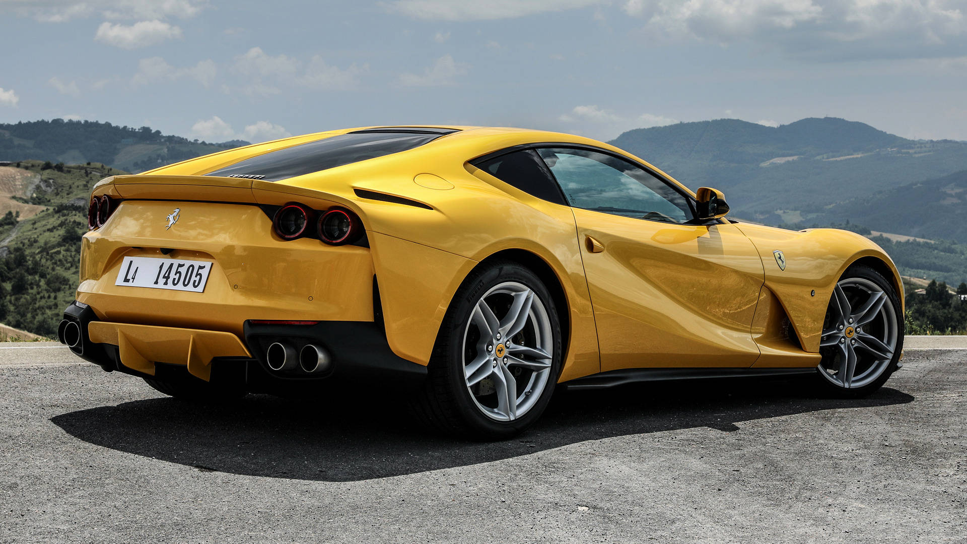 1920x1080 Ferrari 桌布 壁紙 — 一輛鮮黃色的法拉利跑車停在山路上，背景是起伏的山丘和多雲的天空。