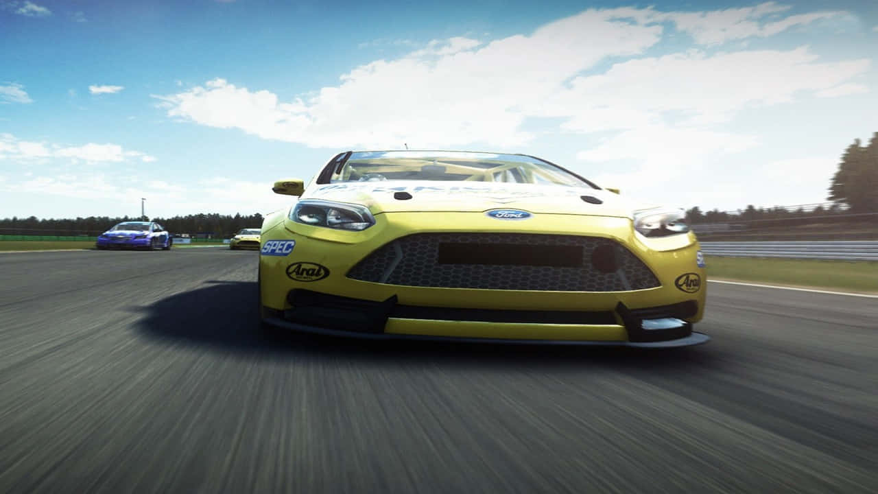 720p Grid Autosport 桌布 壁紙 — 一輛鮮黃色的福特賽車在陽光明媚的賽道上疾馳，背景模糊，頭頂藍天。