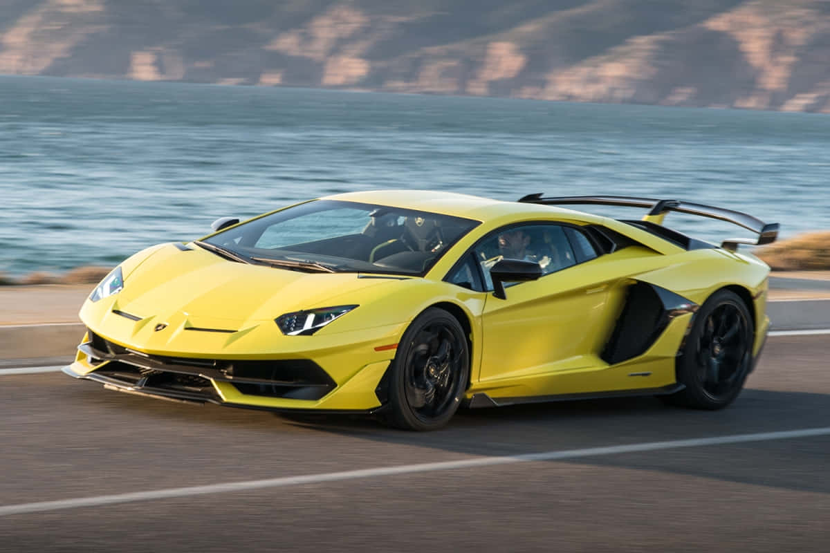Luxury Brands 桌布 壁紙 — 一輛鮮黃色的藍寶堅尼 Aventador 沿著海岸公路疾駛，背景是海洋和懸崖。