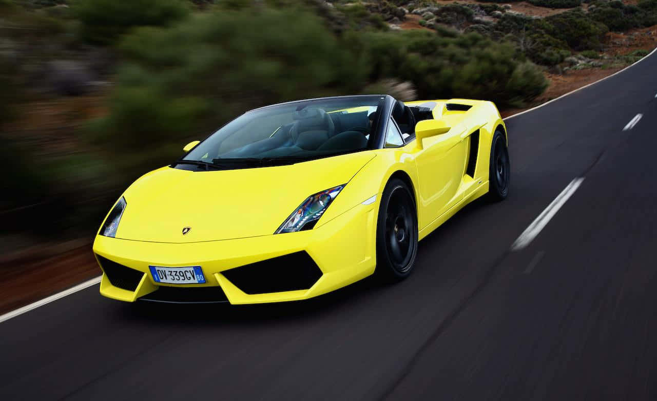 Yellow Car 桌布 壁紙 — 一輛鮮黃色的藍寶堅尼 Gallardo Spyder 在蜿蜒的山路上疾馳，周圍的綠化模糊不清。