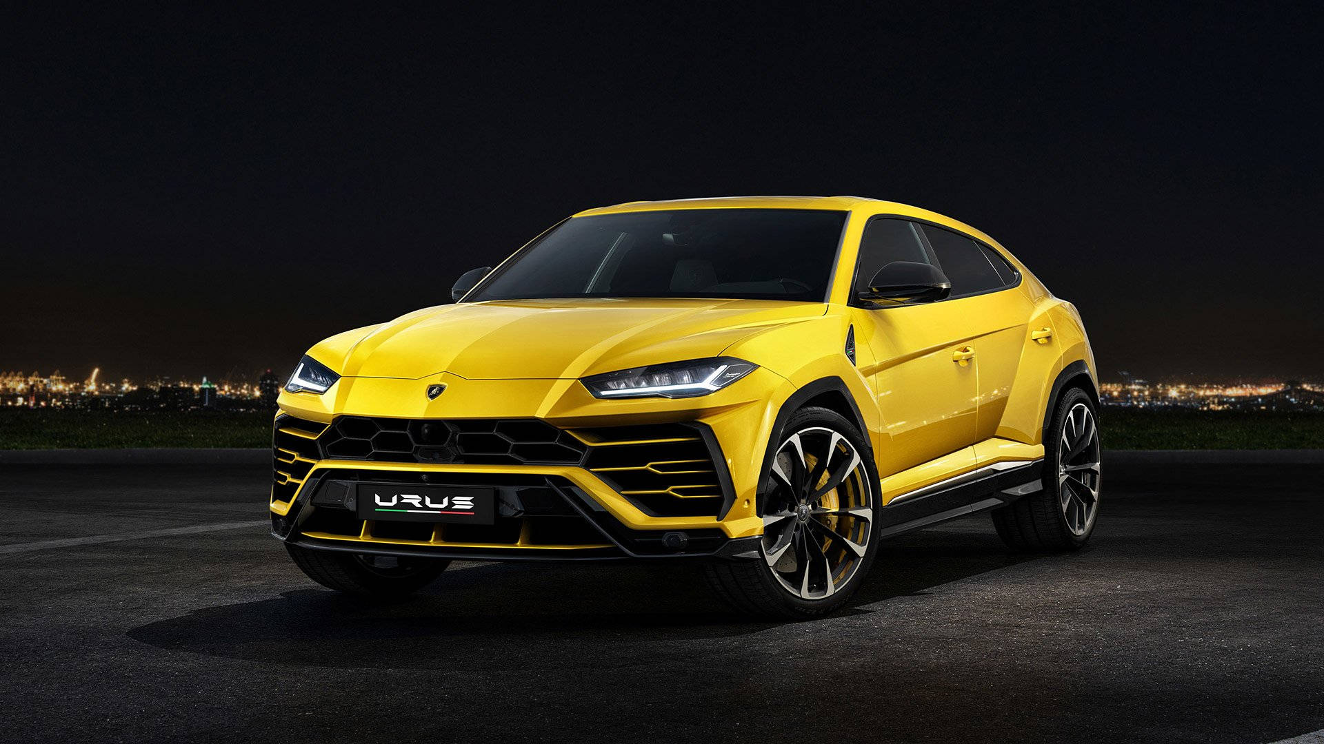lambo 桌布 壁紙 — 一輛鮮黃色的藍寶堅尼 Urus SUV 在夜燈下閃耀，背景是閃爍的城市天際線。