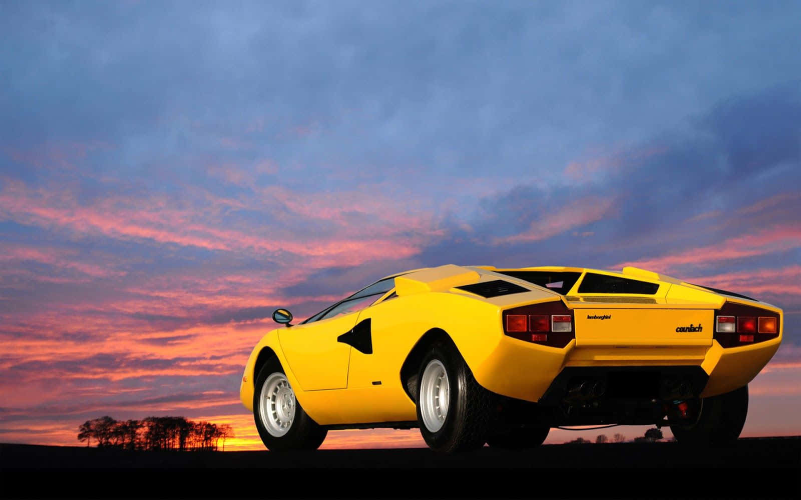 Lamborghini Countach 桌布 壁紙 — 一輛鮮黃色的藍寶堅尼Countach停泊在日落時分的山丘上，上方有火熱的橙色和紫色雲彩。