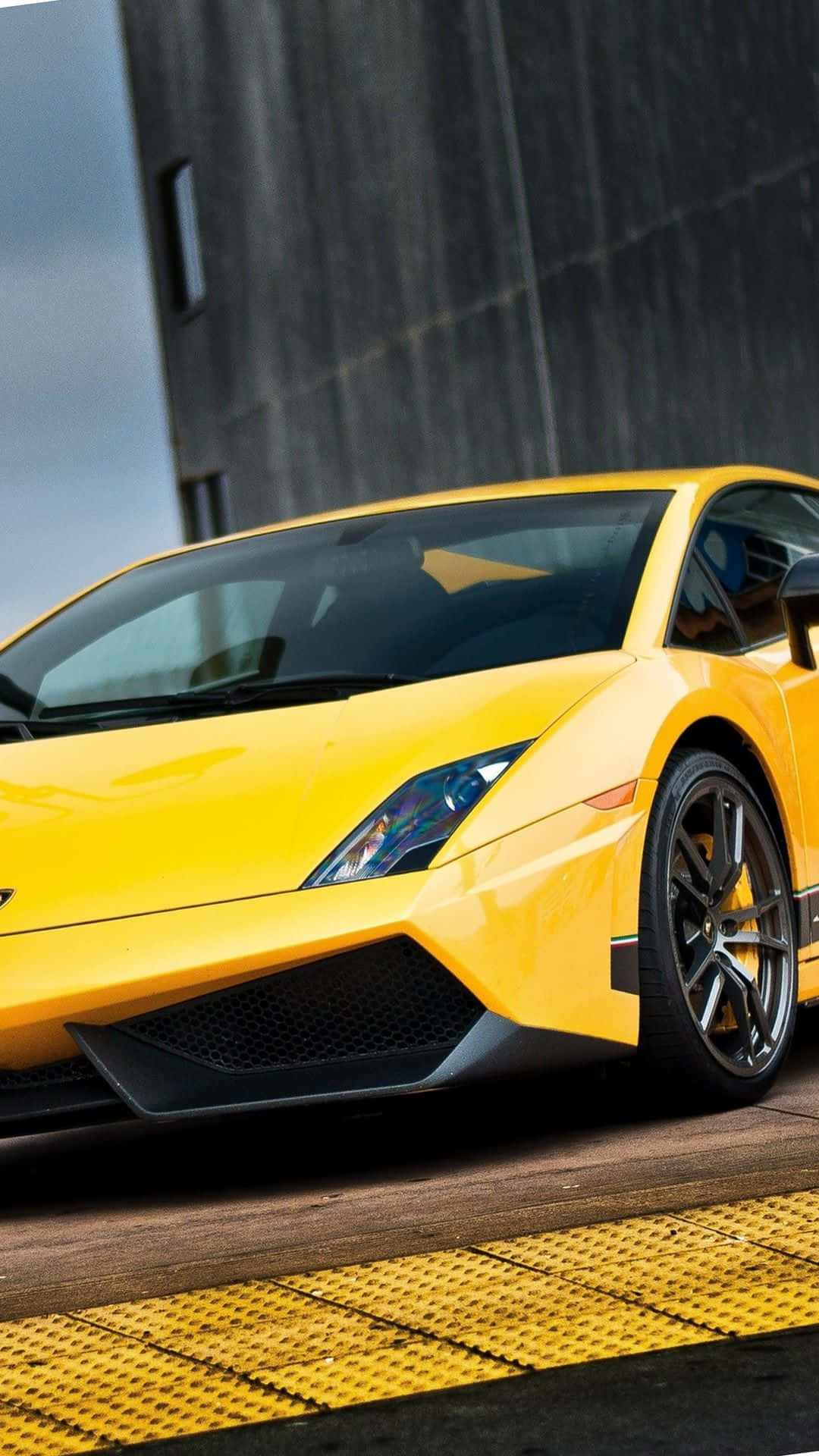 Lamborghini Phone 桌布 壁紙 — 一輛鮮黃色的藍寶堅尼Gallardo跑車停放在黃色紋理平台上，背景是深色混凝土牆。