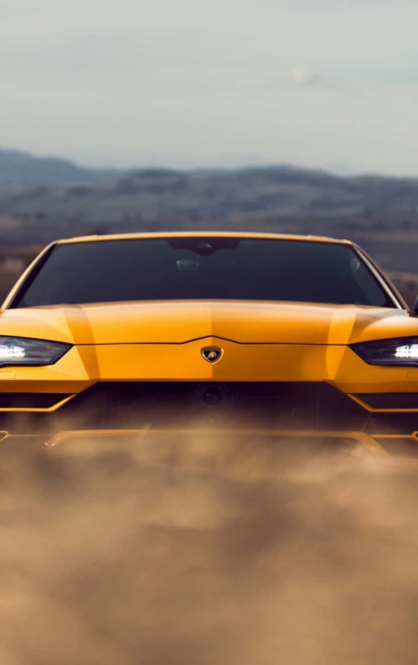 Pixel 3xl Lamborghini 桌布 壁紙 — 一輛鮮黃色的藍寶堅尼在塵土飛揚的地形上奔馳，揚起塵雲，背景是朦朧的山脈。
