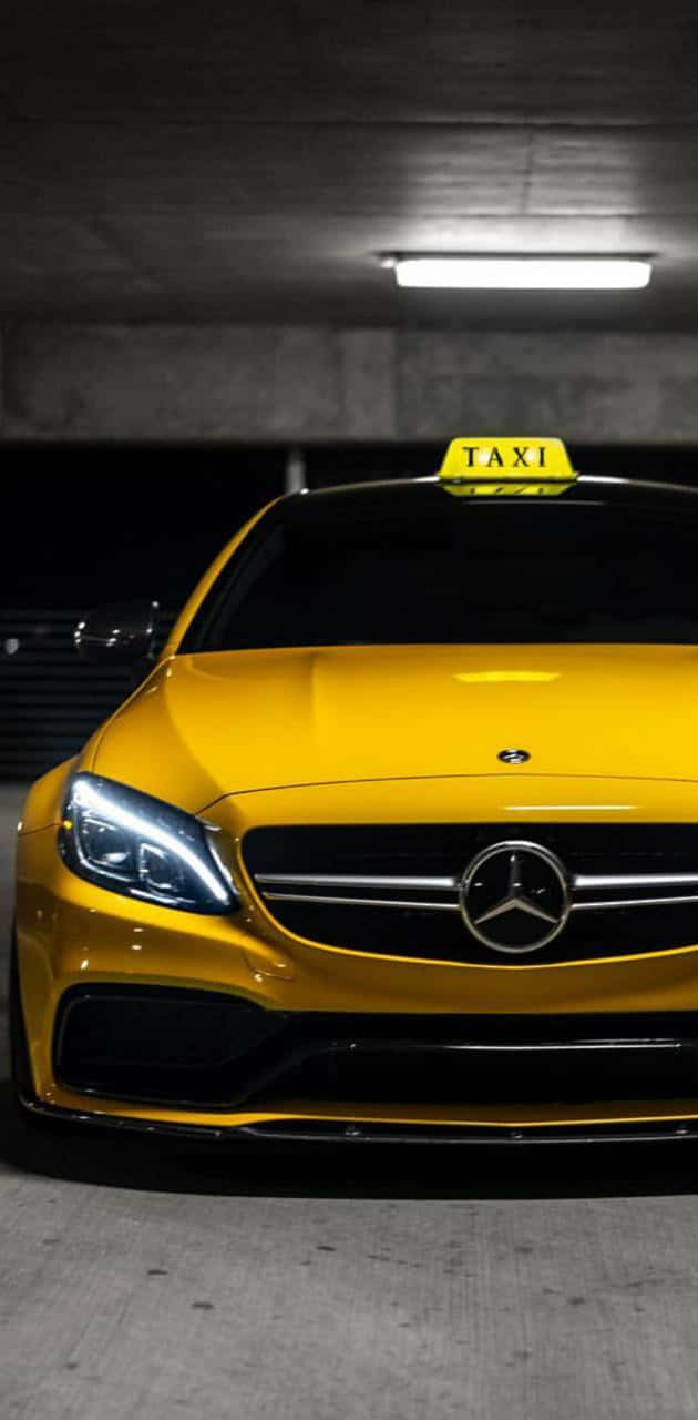 Yellow Cab 桌布 壁紙 — 一輛鮮黃色的賓士計程車在昏暗的混凝土停車場中，在螢光燈下閃閃發光。