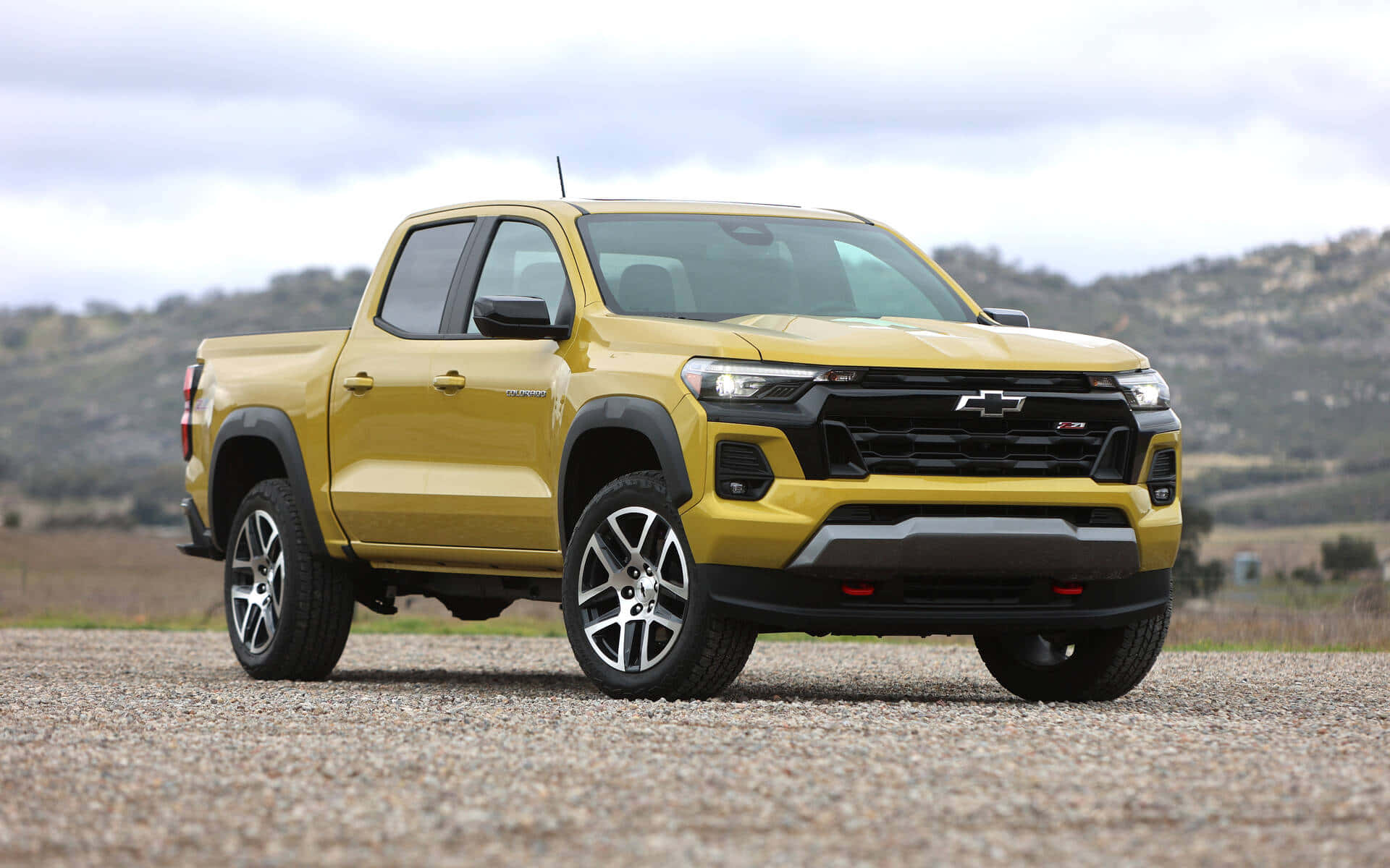 Chevrolet 桌布 壁紙 — 一輛鮮黃色的雪佛蘭Colorado ZR2皮卡車大膽地停在碎石地上，背景是起伏的丘陵，天空多雲。