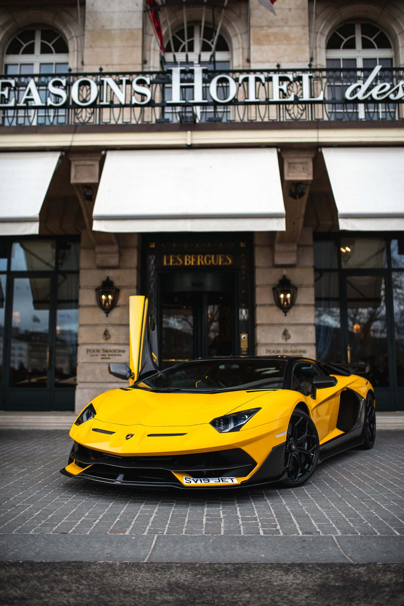 race car 桌布 壁紙 — 一輛鮮黃色藍寶堅尼 Aventador 配備鷗翼車門，停泊在豪華飯店門前的鵝卵石路上。