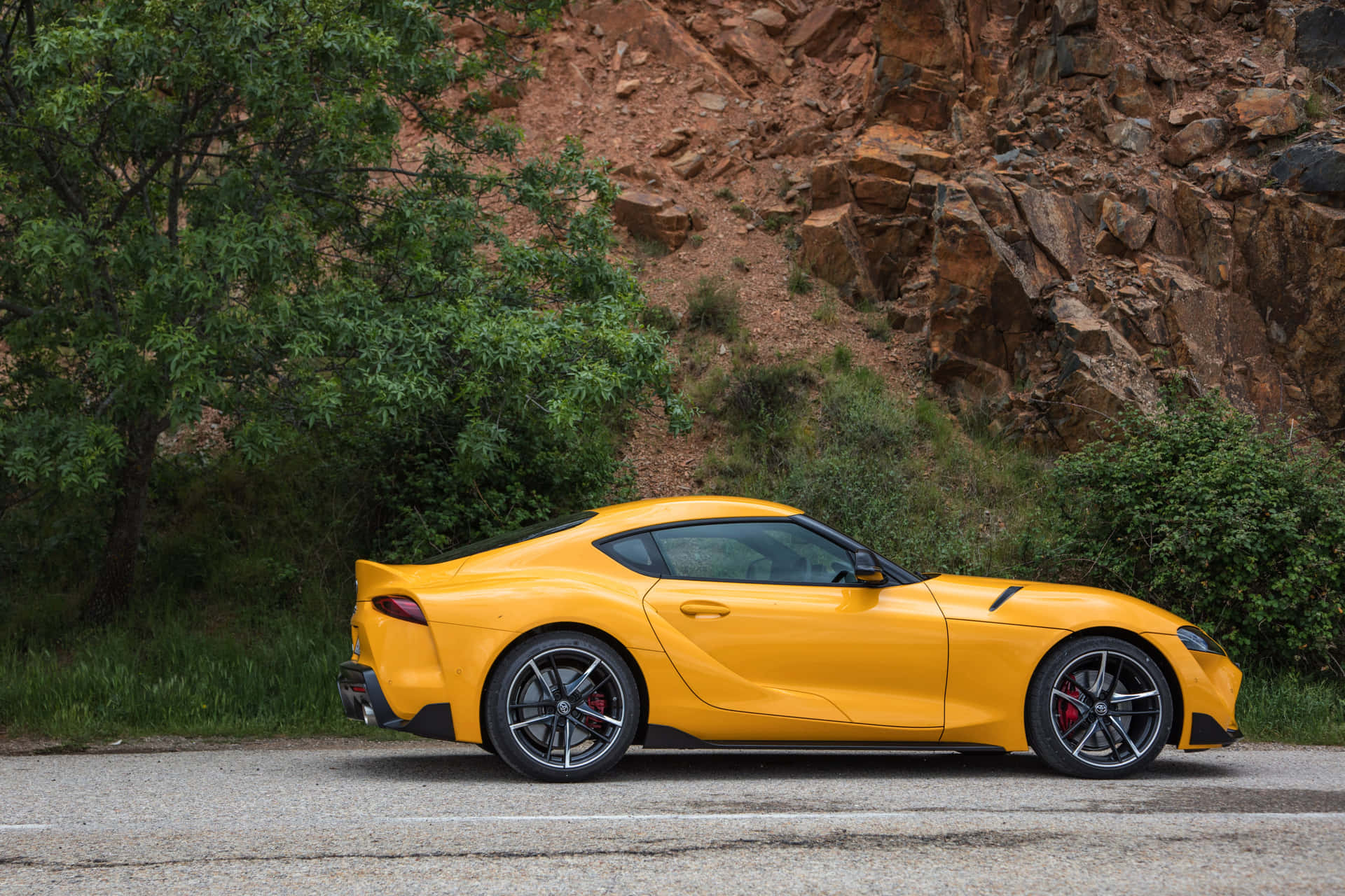 黃色跑車停泊在碎石路上，靠近岩石峭壁和樹木。 — Toyota Supra Mk4 壁紙