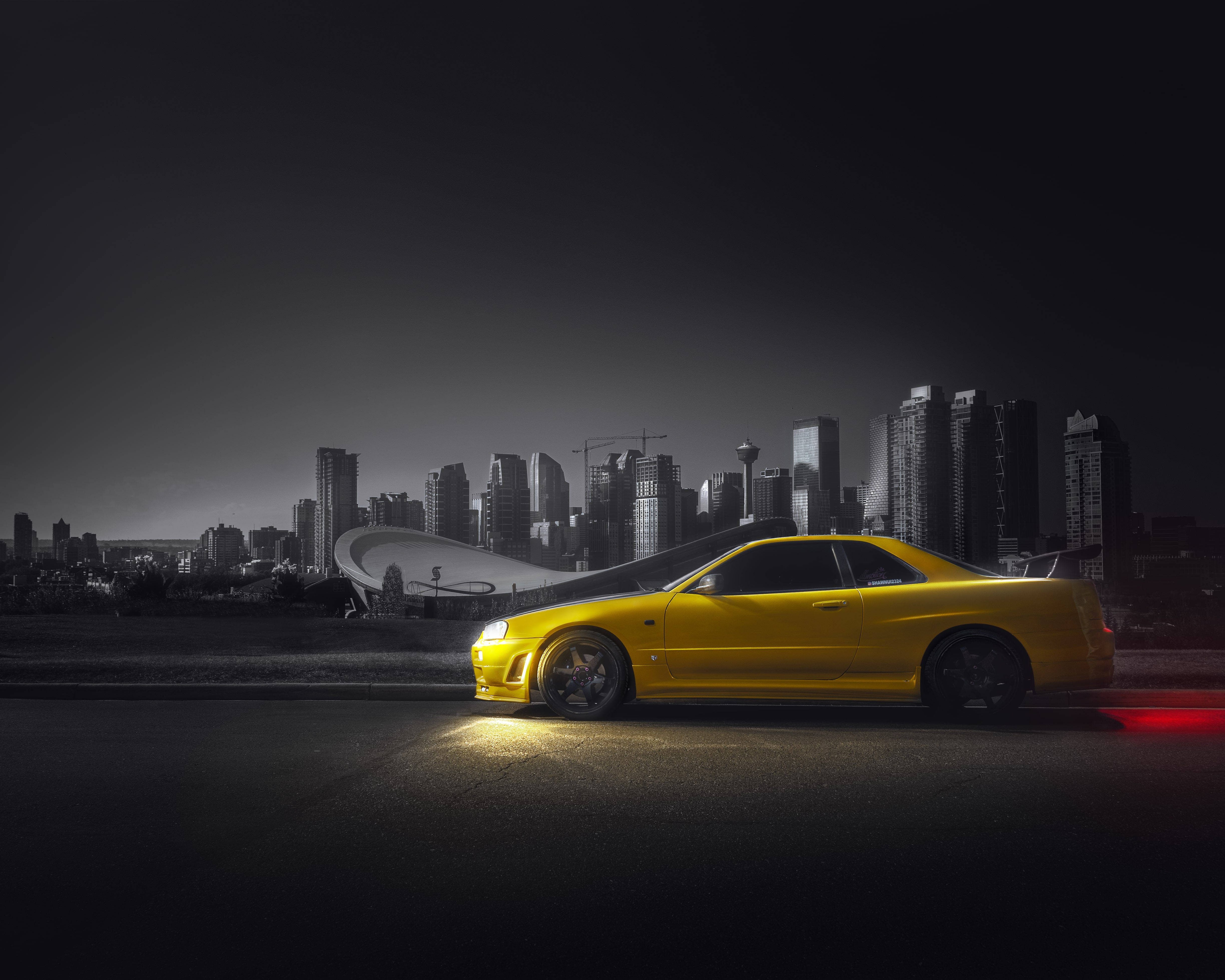 Nissan Skyline 桌布 壁紙 — 一輛鮮黃色跑車在夜間單色城市天際線背景下，於街燈下閃耀。