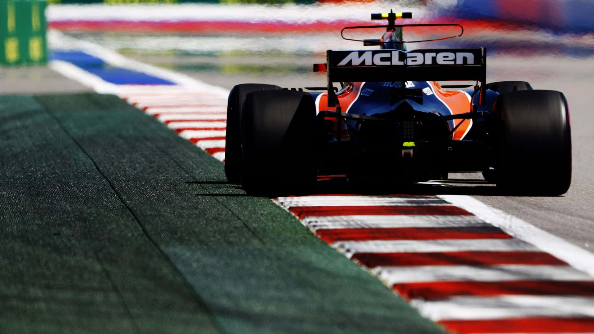 Formula One 桌布 壁紙 — 一輛麥拉倫一級方程式賽車在明亮的日光下，沿著一條以紅、白、綠色路緣石為邊界的賽道奔馳。